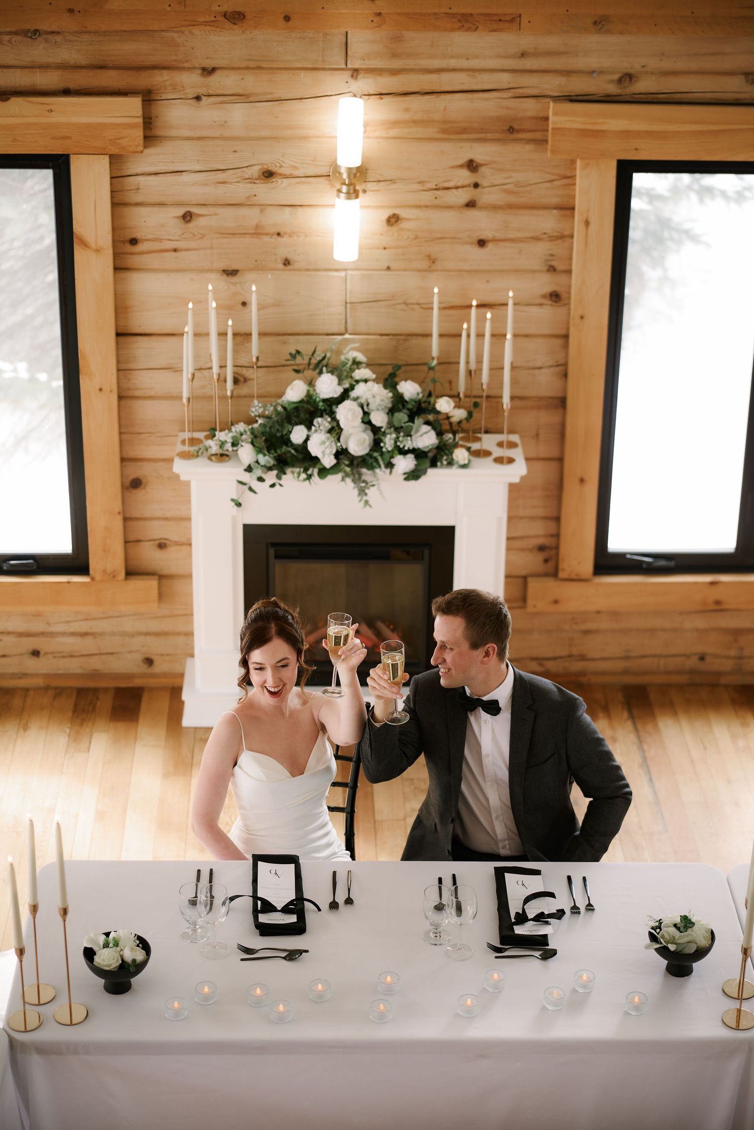 Newlyweds toast at their reception table in a rustic wooden venue with elegant white floral decorations.