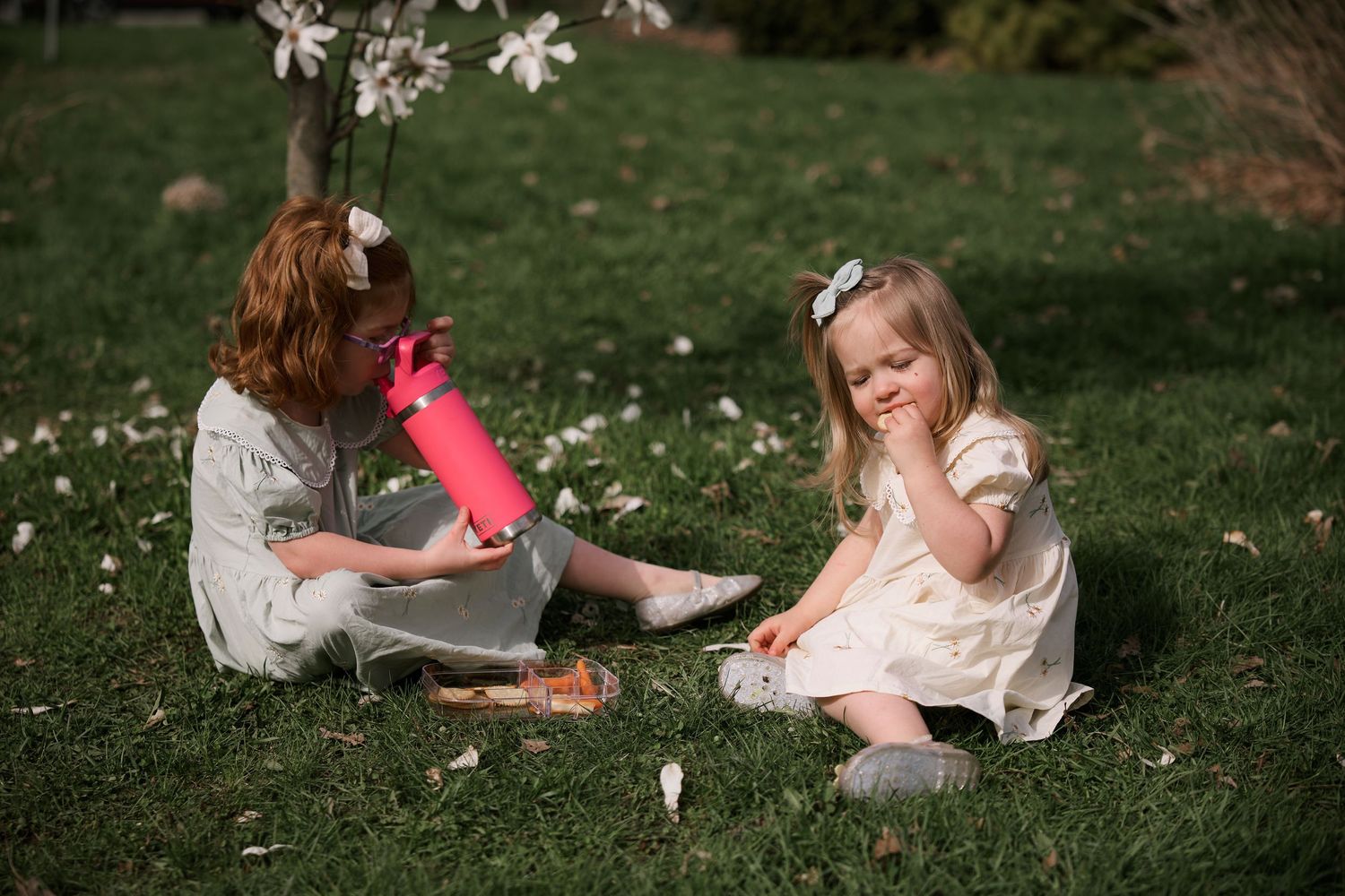Two children sitting on grass playing with pink toys among spring flowers.