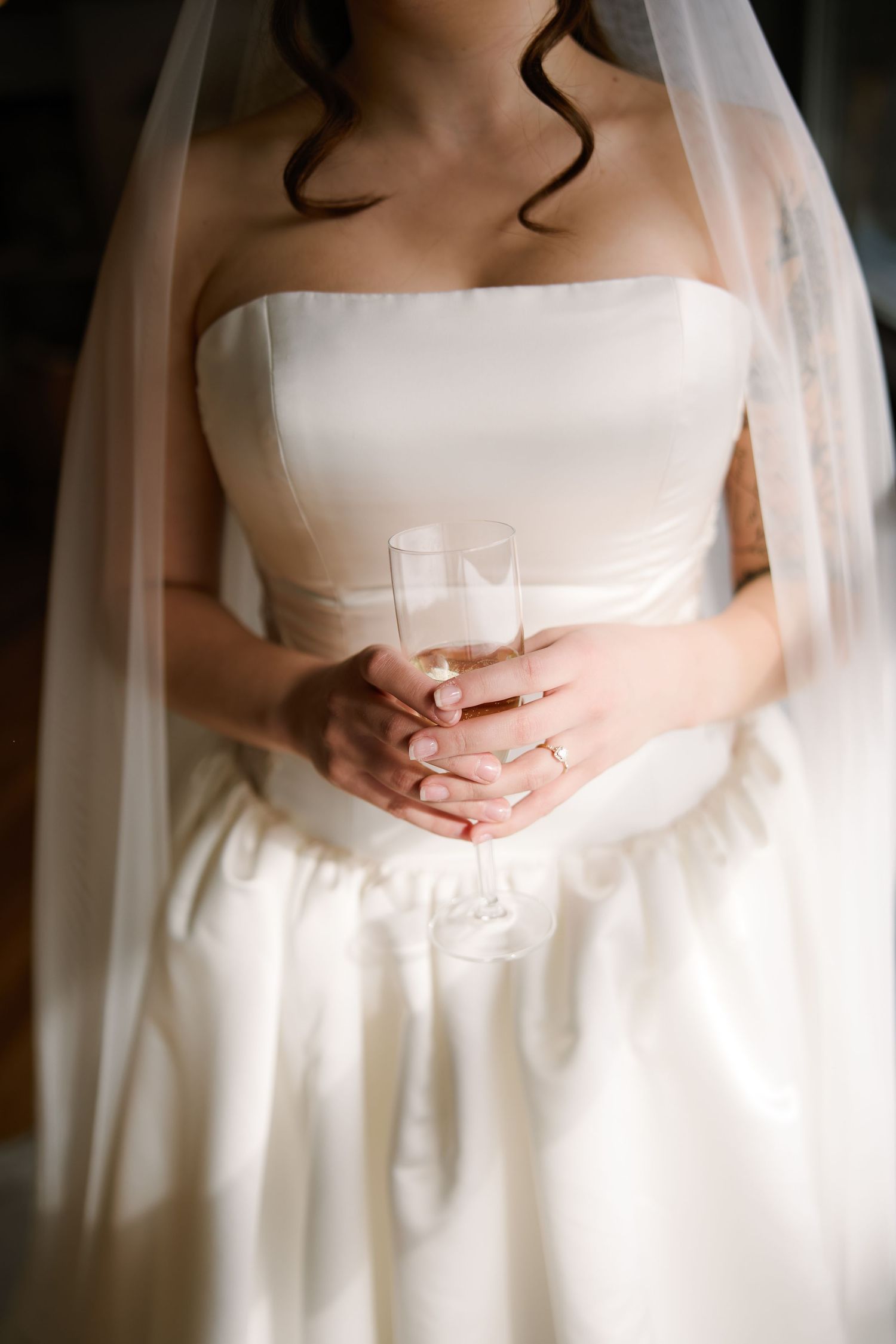 Minimalist bridal portrait focusing on white wedding dress and clasped hands.