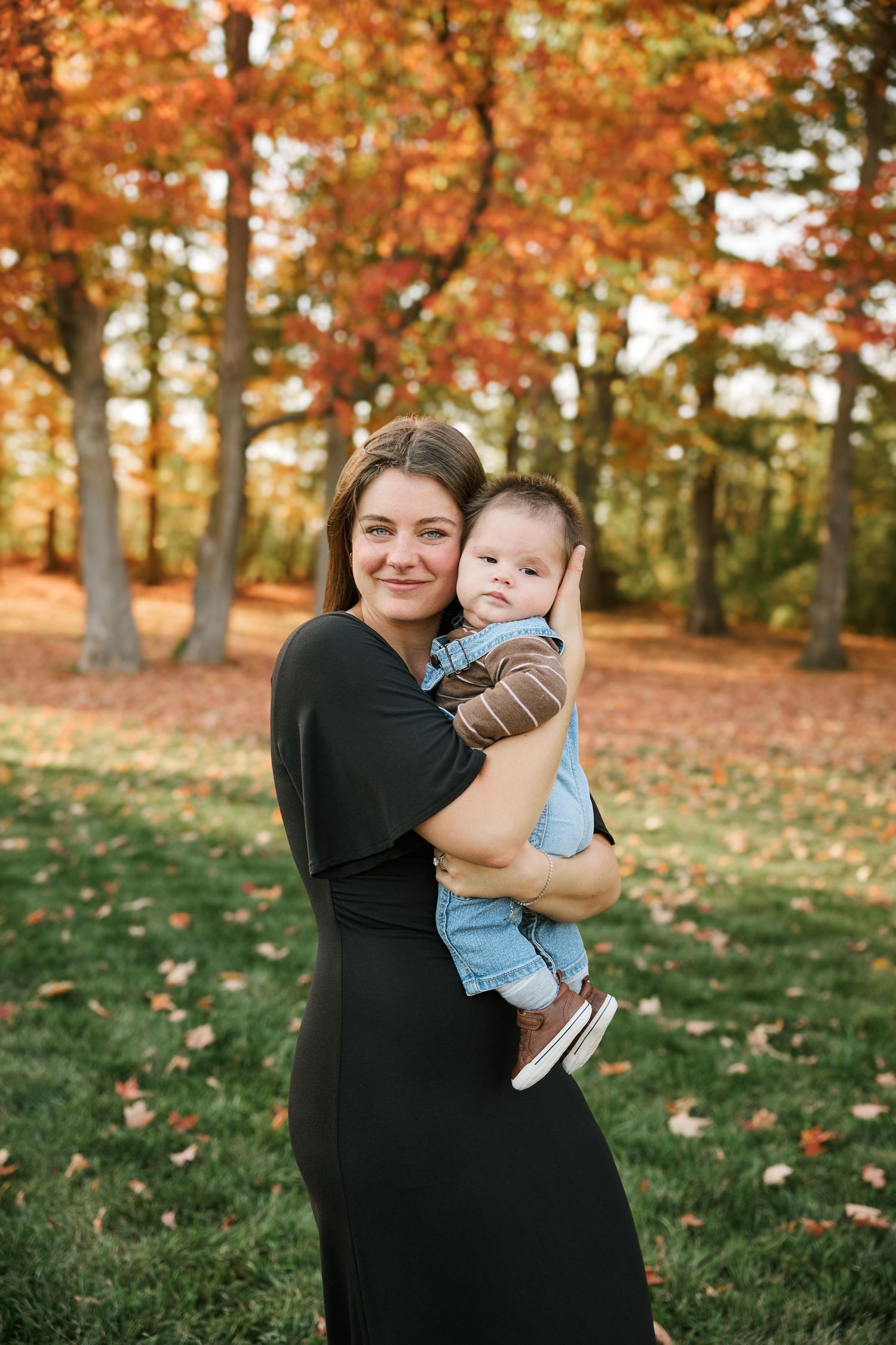 Autumn photoshoot in park with vibrant orange fall foliage in background.