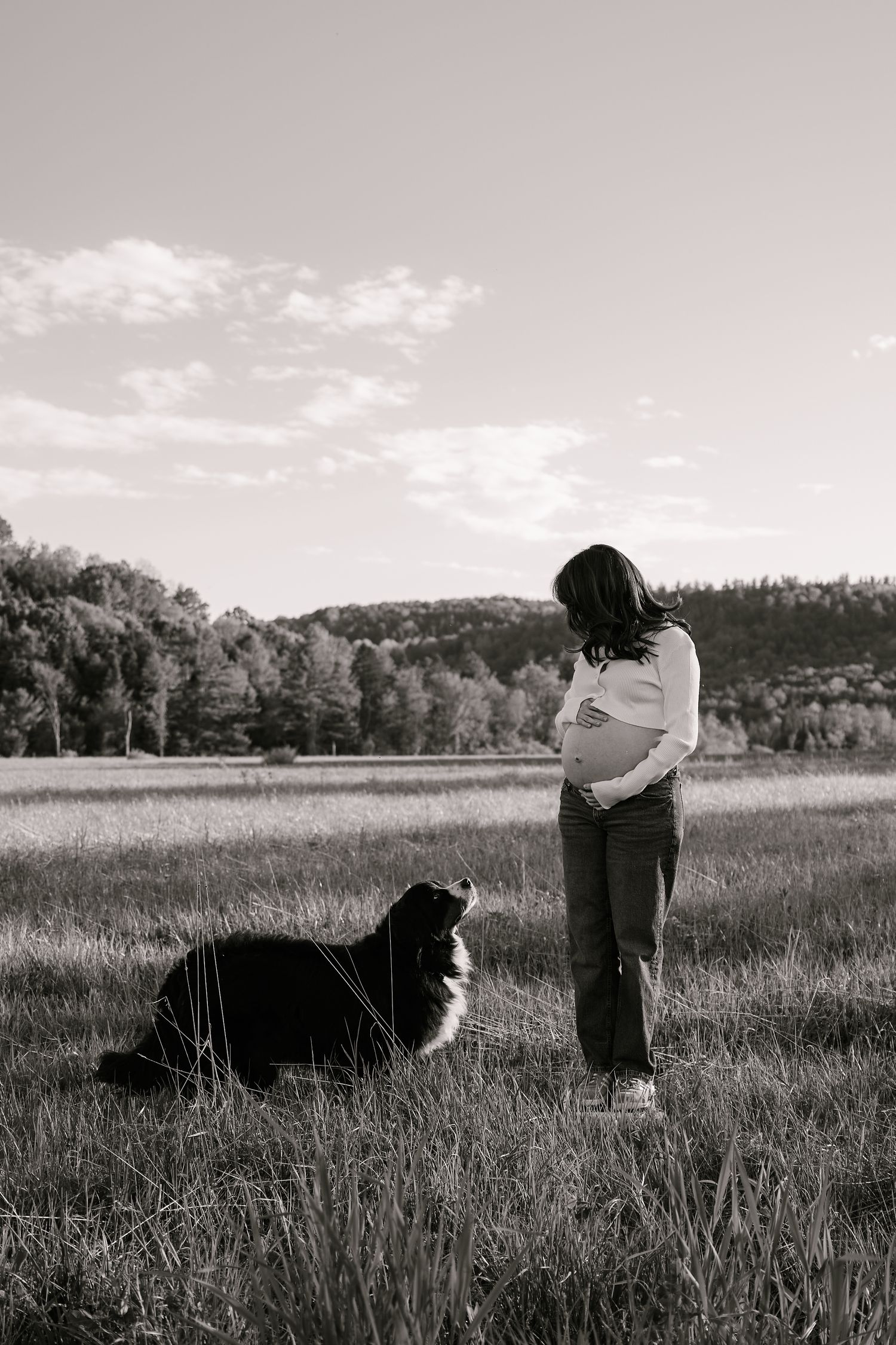 A person stands in a grassy field with a black and white border collie on an overcast day.