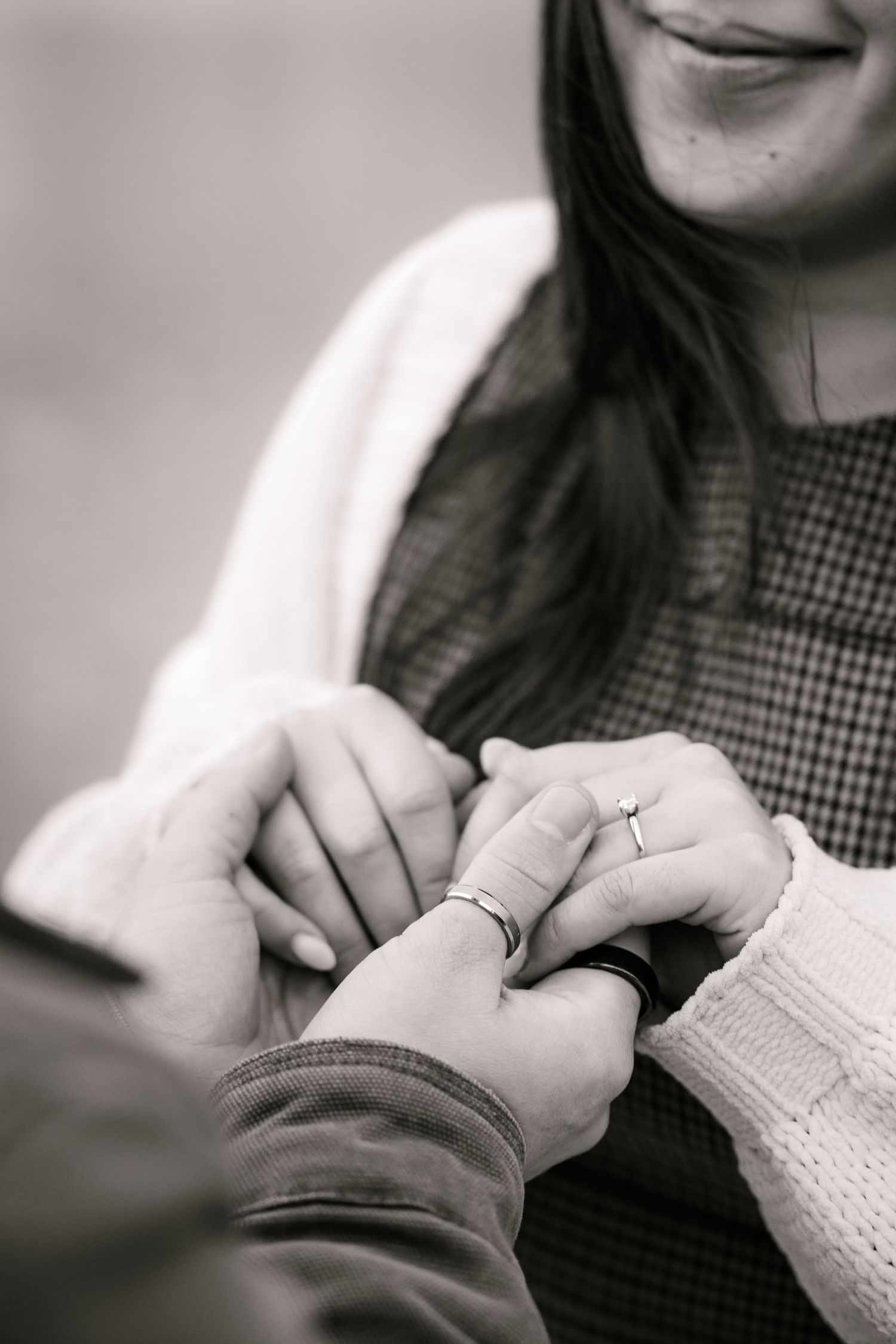 Black and white photo of a couple holding hands, woman smiling with an engagement ring on her finger.