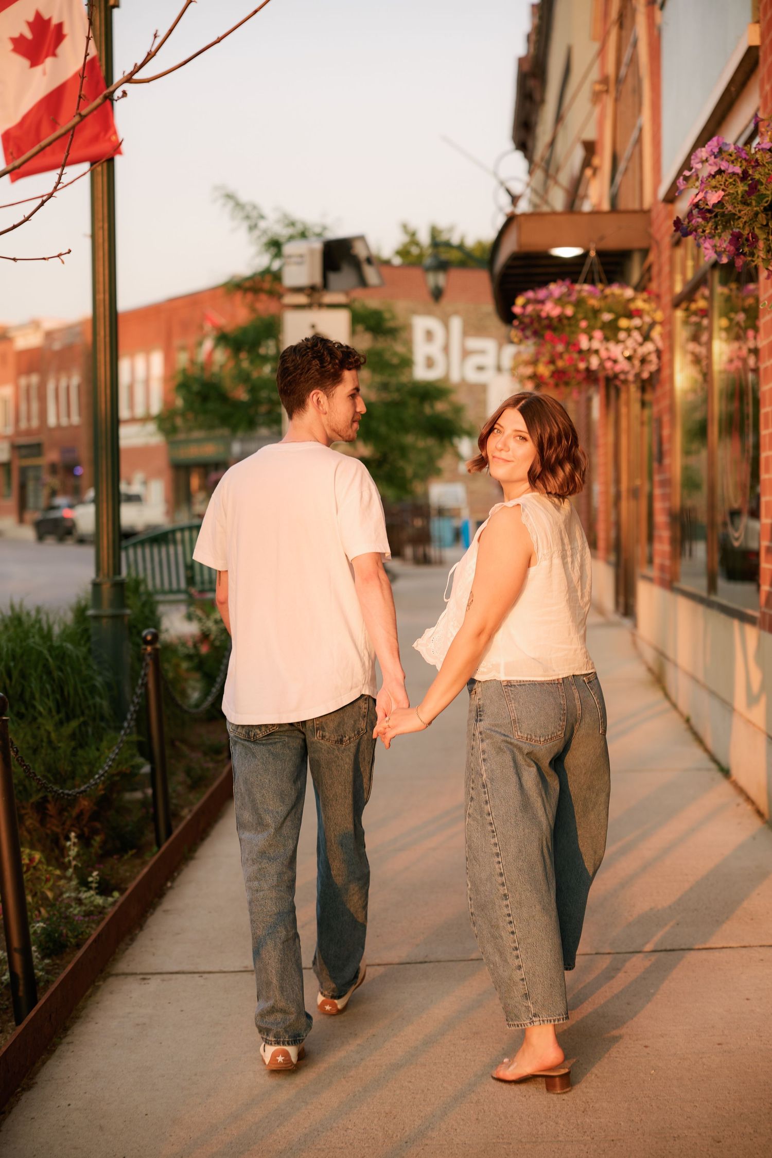 Couple holding hands walking down sunny small-town sidewalk at golden hour.