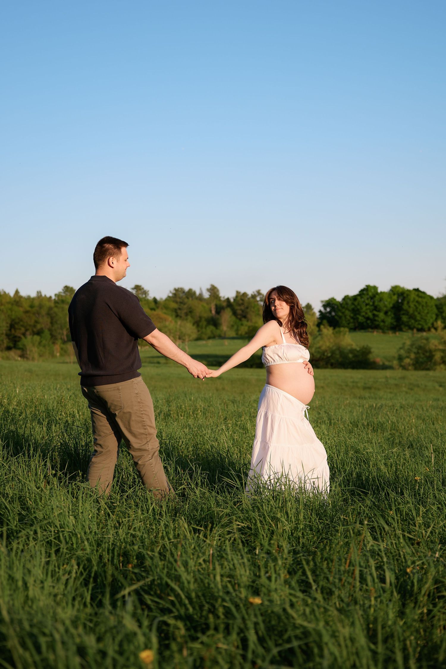 Playful couple dancing in a sunlit meadow during their wedding photoshoot.