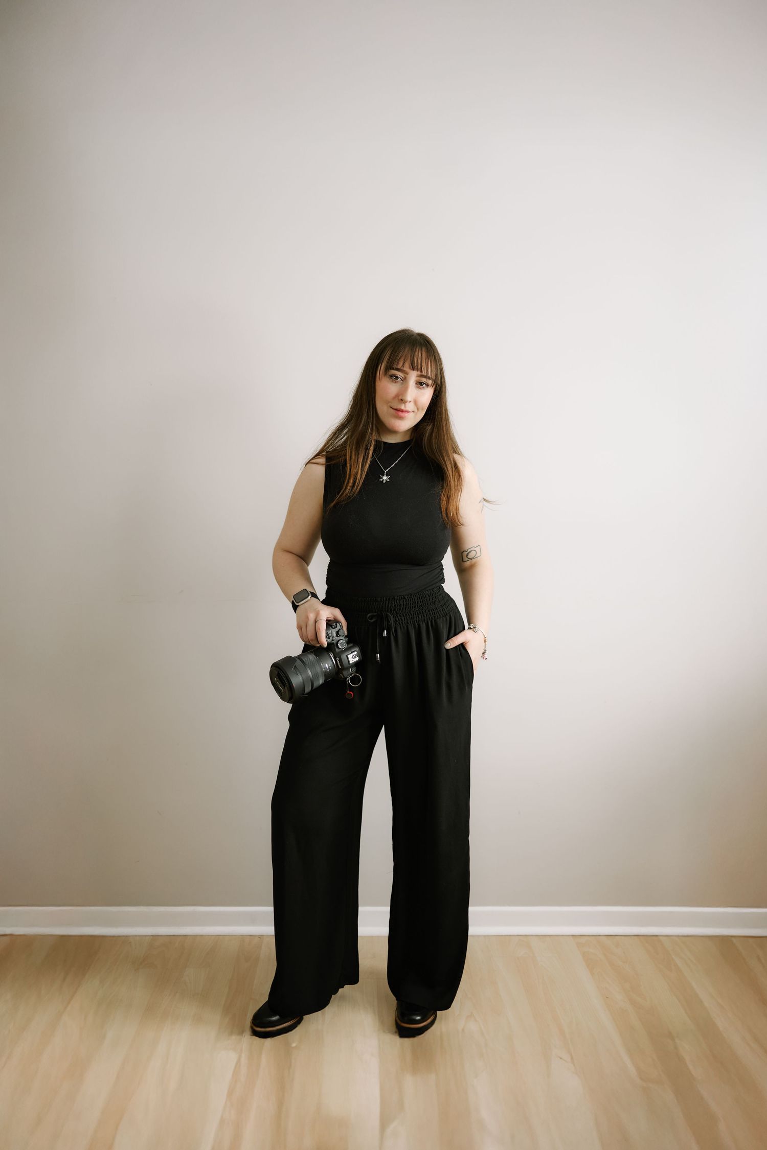 Photographer in black attire demonstrating various poses with camera equipment.