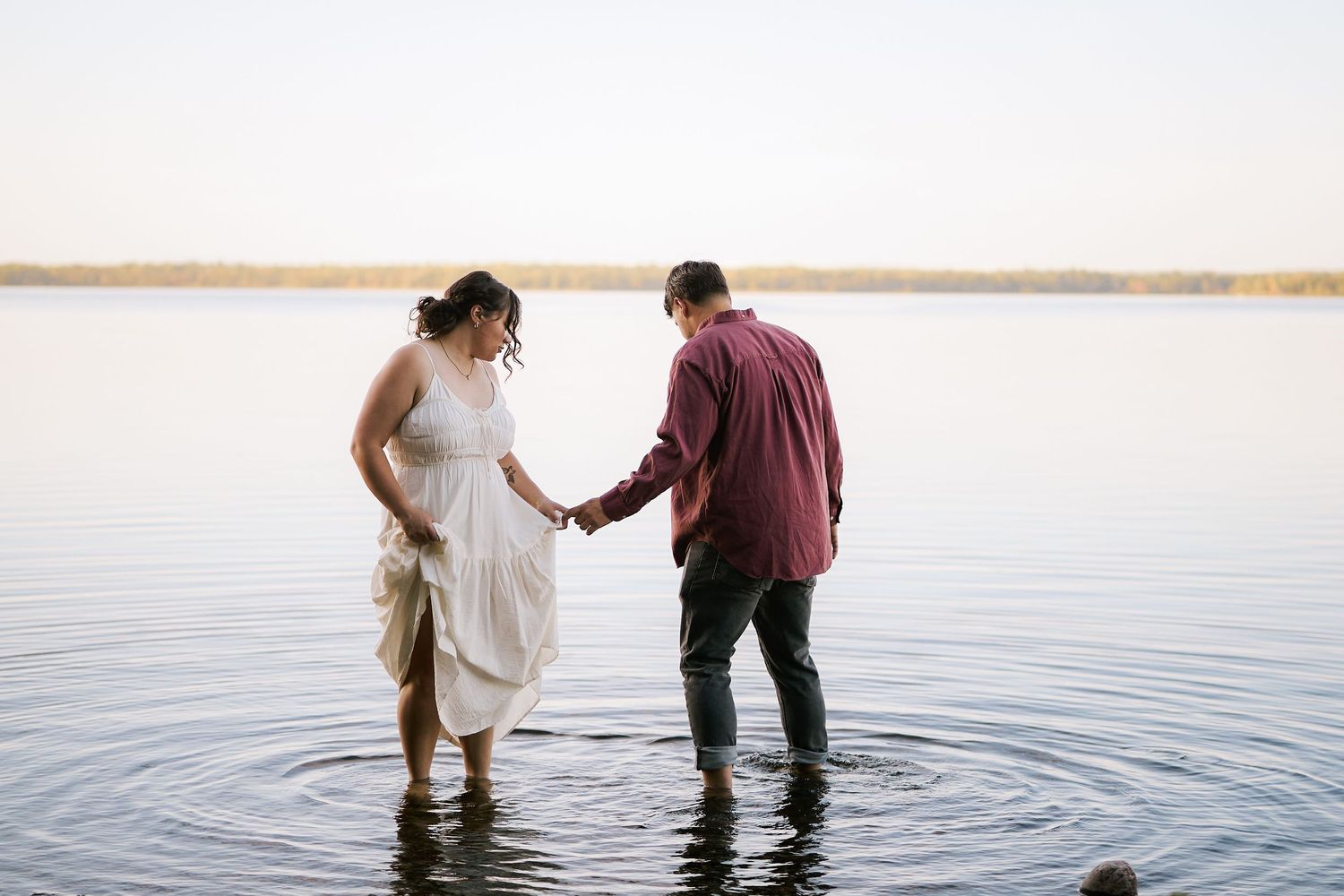 Romantic sequence of a couple wading into calm lake waters at golden hour.