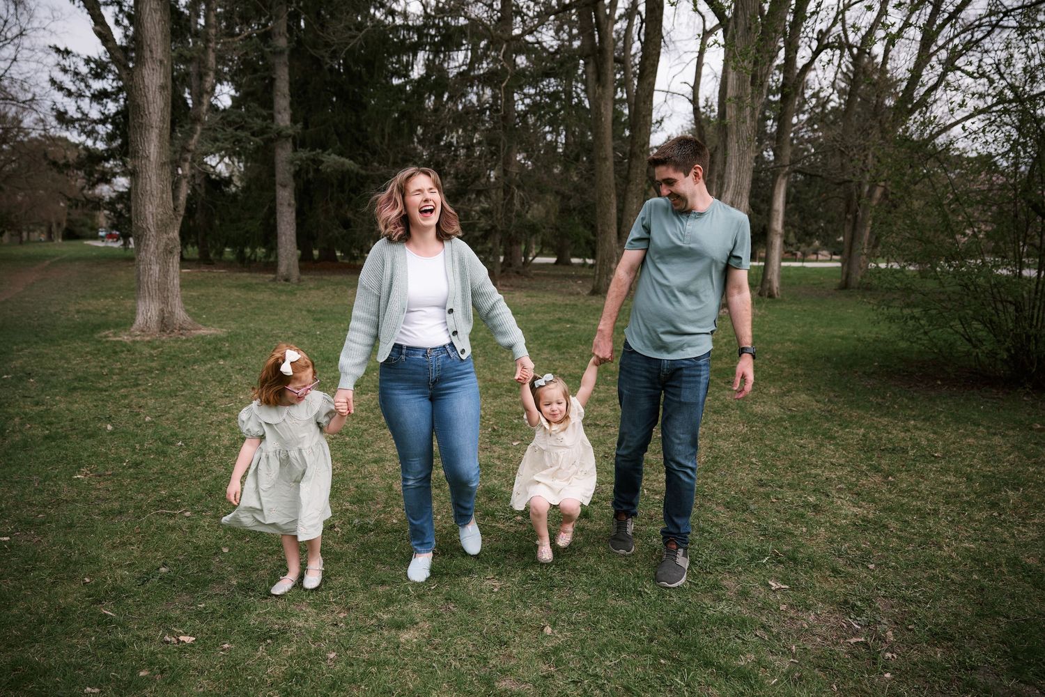 Family walking together through a park with tall trees in the background.