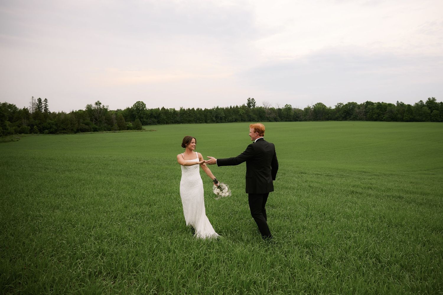 A couple stands together in a vast green field during their wedding.