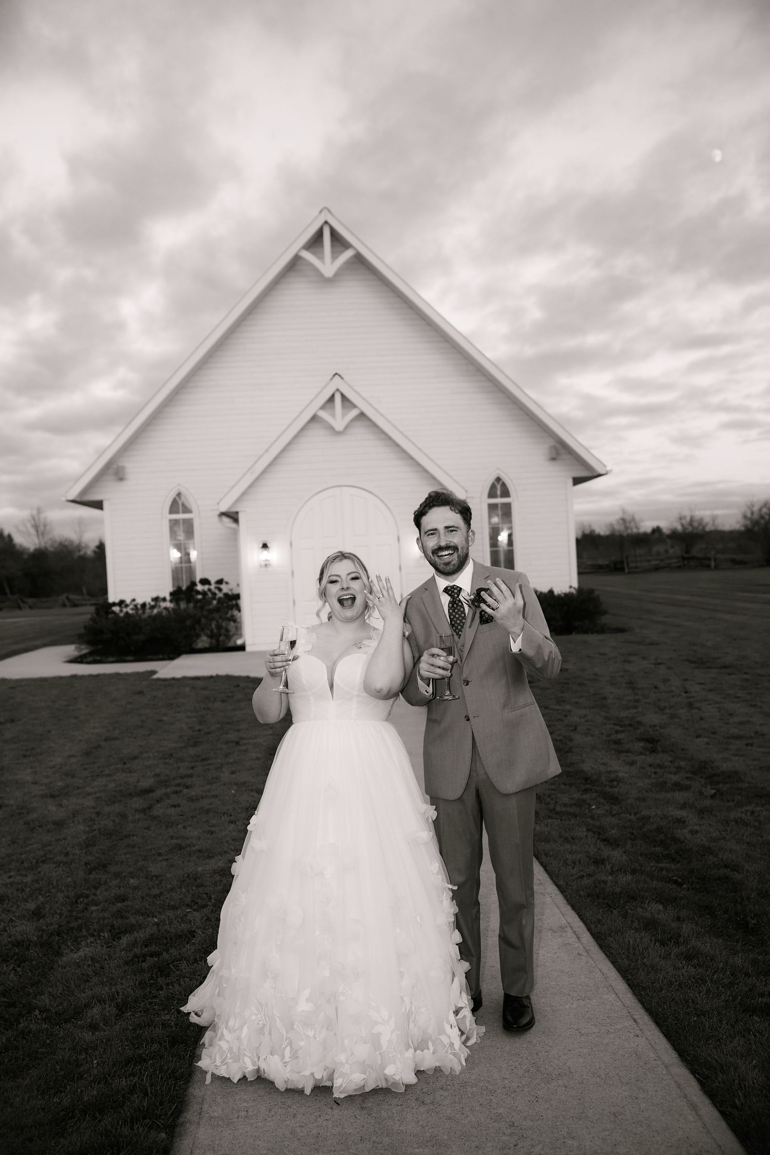Wedding couple walking and laughing together outside a white chapel building.