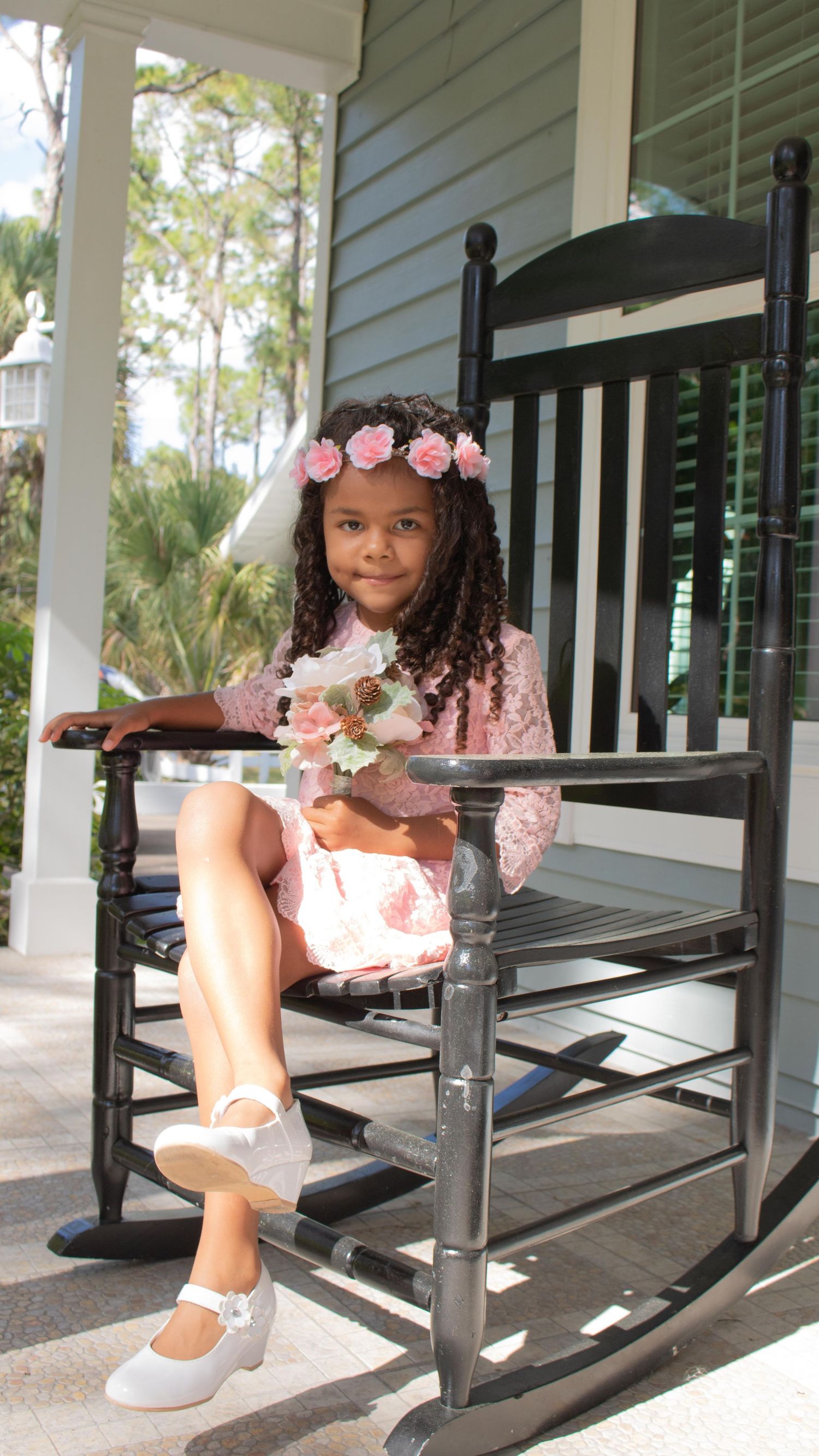 A person in pink sits on a wooden bench wearing a floral crown in a serene outdoor setting.