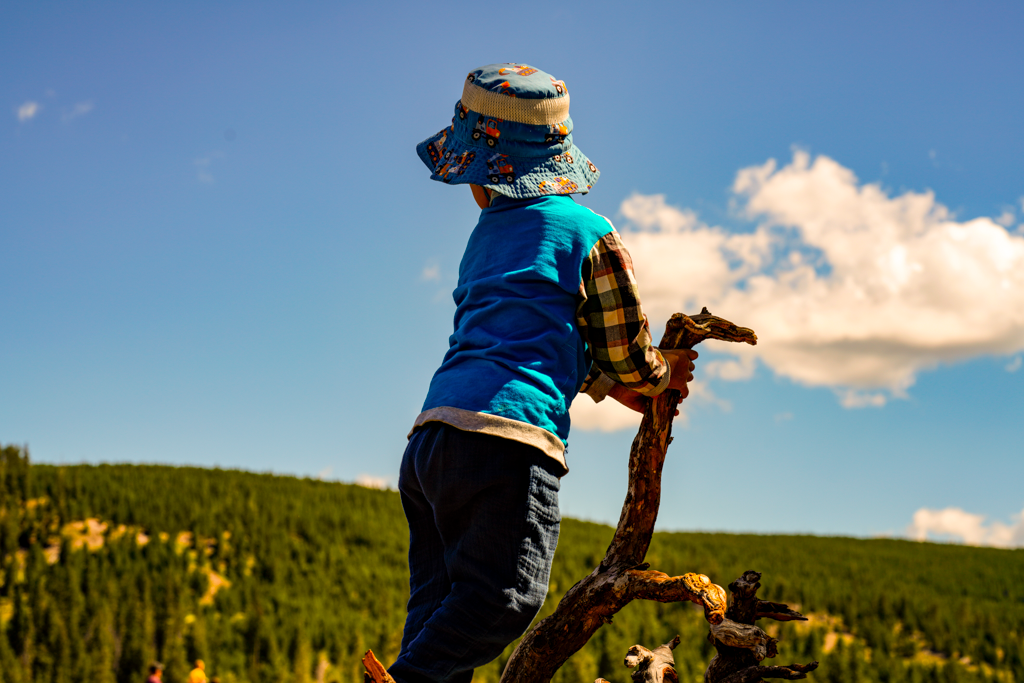 Person wearing blue clothing and hat stands against mountain landscape backdrop.