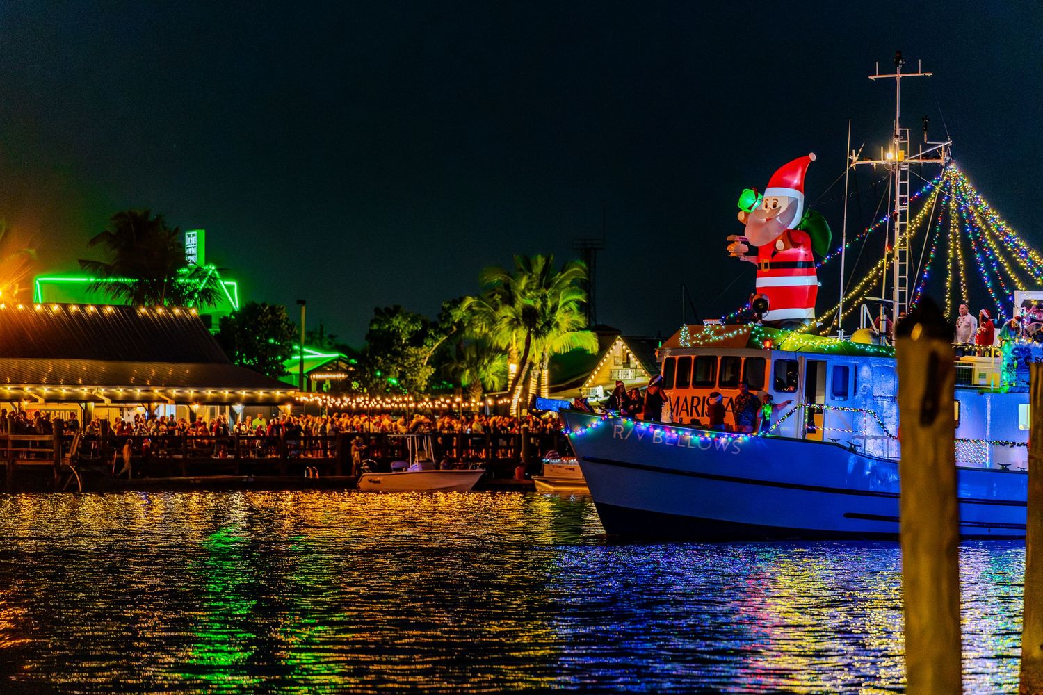 A festive boat decorated with Christmas lights and Santa Claus figure docked at night with colorful reflections on the water.