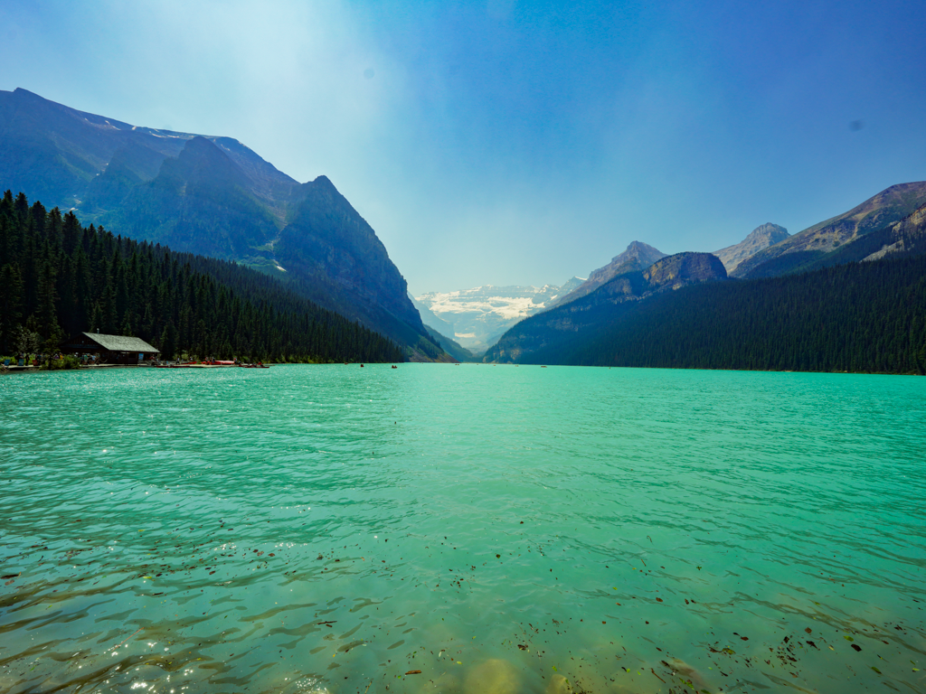Turquoise lake waters surrounded by mountain peaks and forest in a scenic landscape.