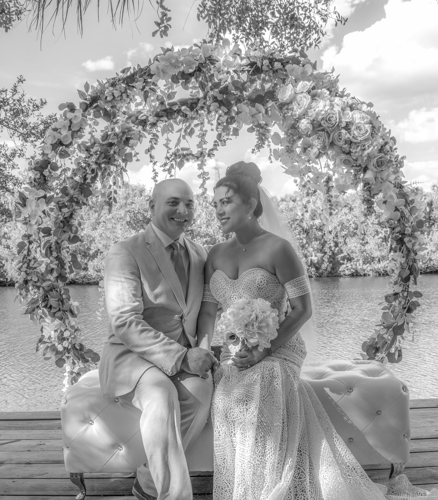 Newlyweds sharing joyful moments by the waterfront in black and white photography.