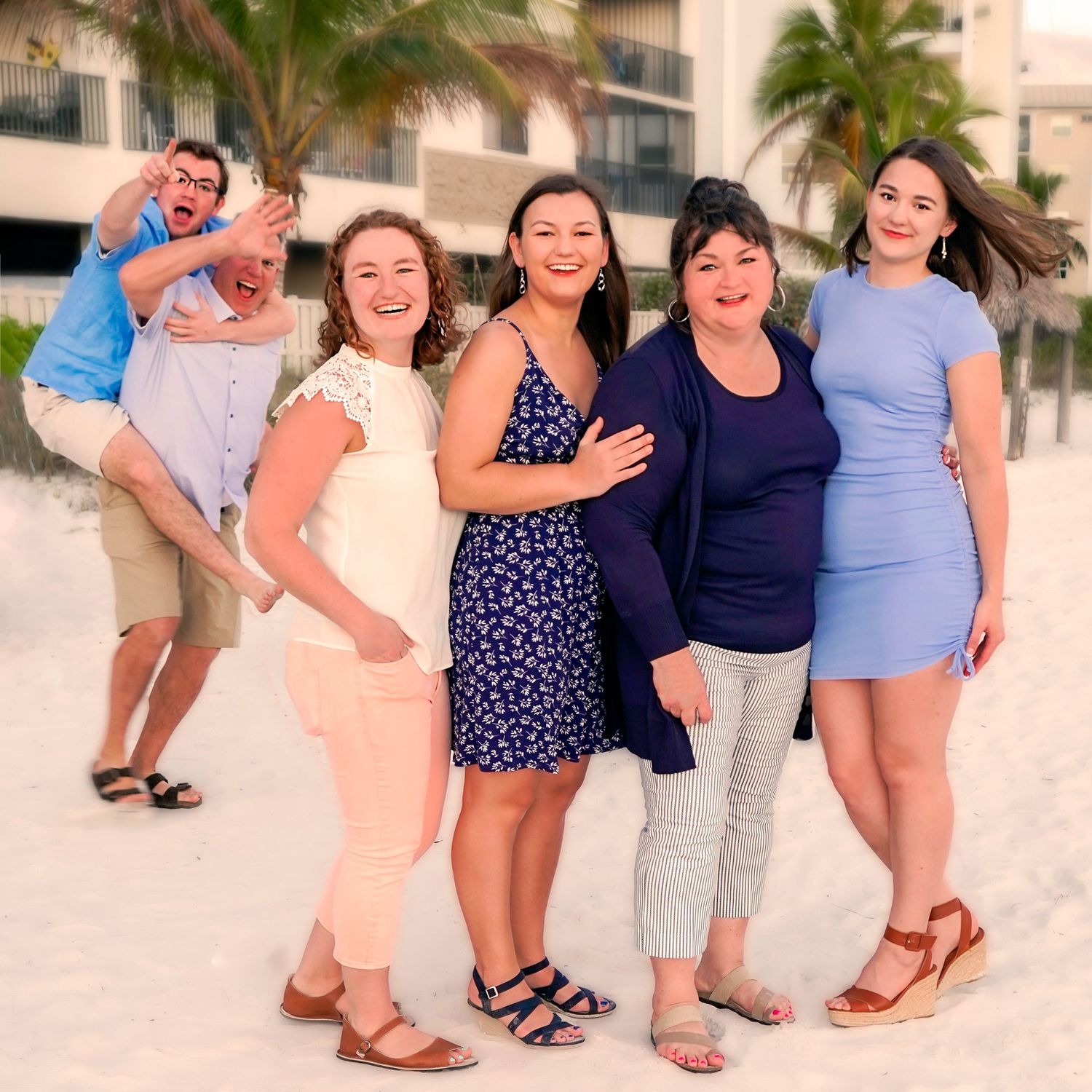 Group enjoying sunset on white sandy beach with palm trees in background.