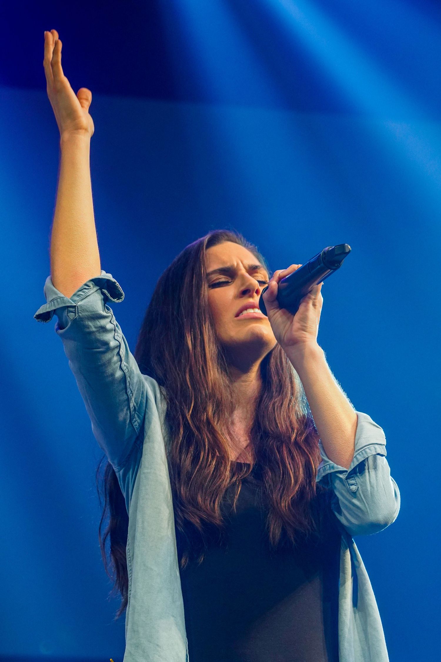 Singer performing passionately on stage under dramatic blue lighting.