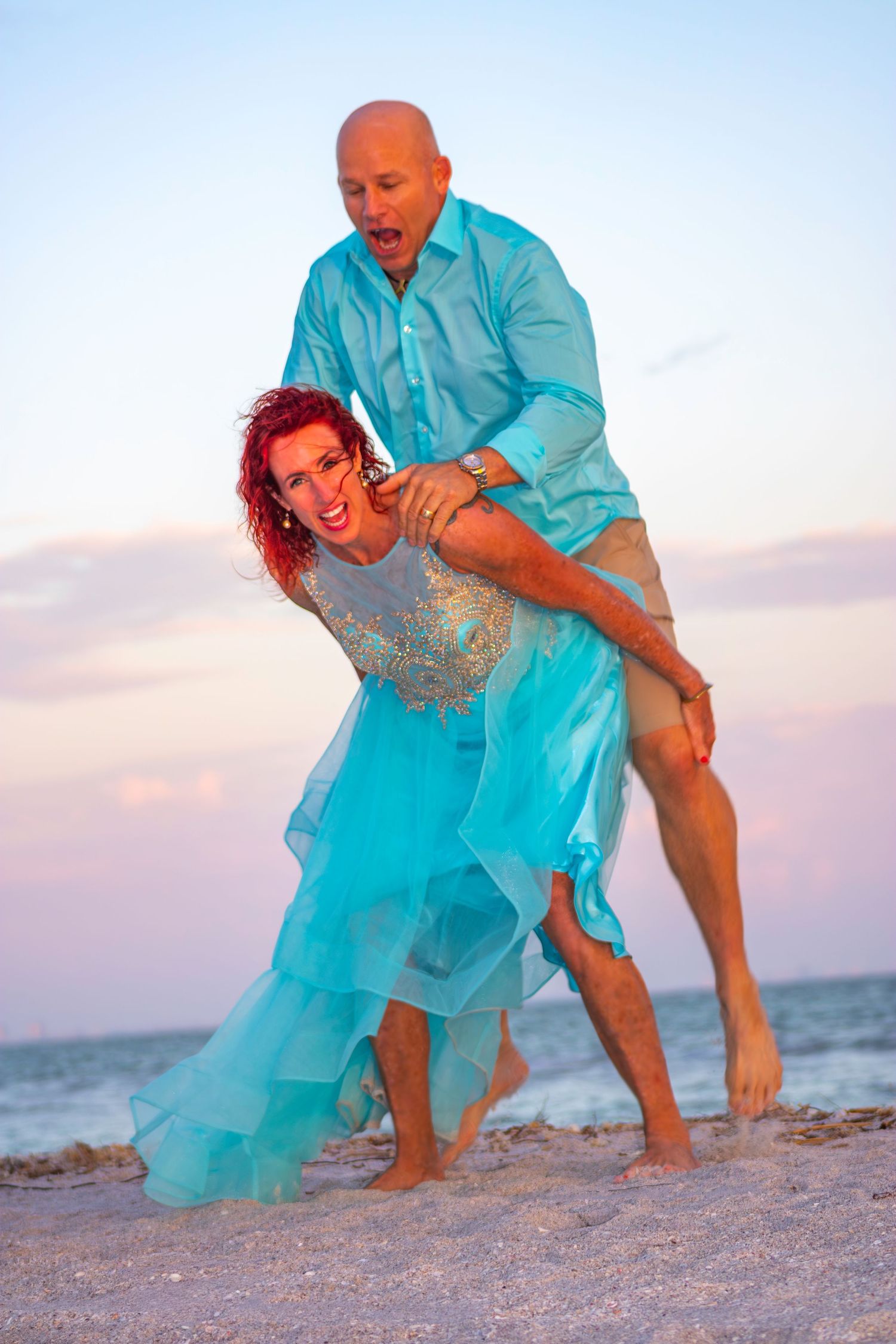 A playful beach scene with two people in turquoise clothing interacting on the sand.