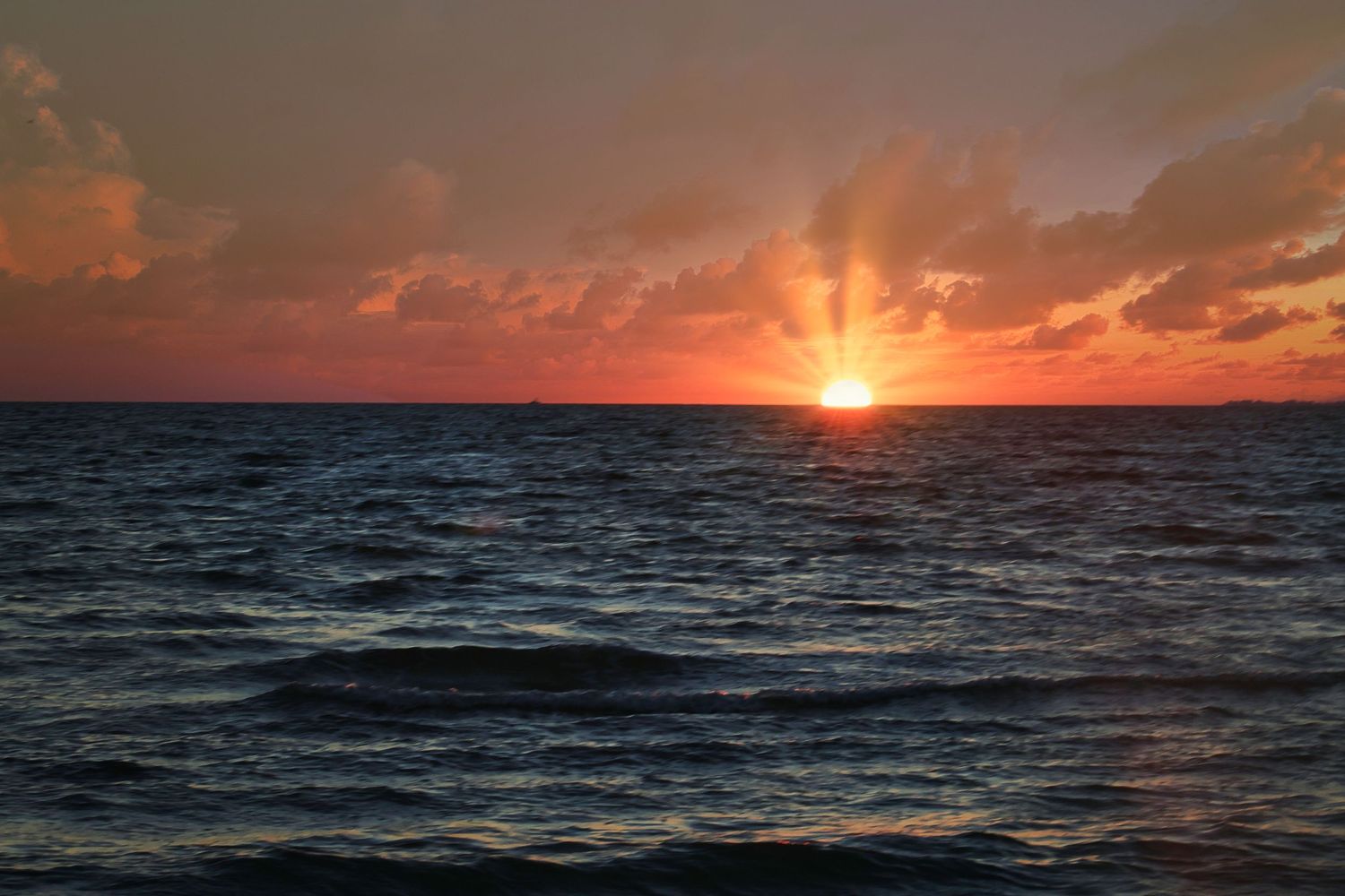 A dramatic ocean sunset with vibrant orange sky and dark rolling waves.