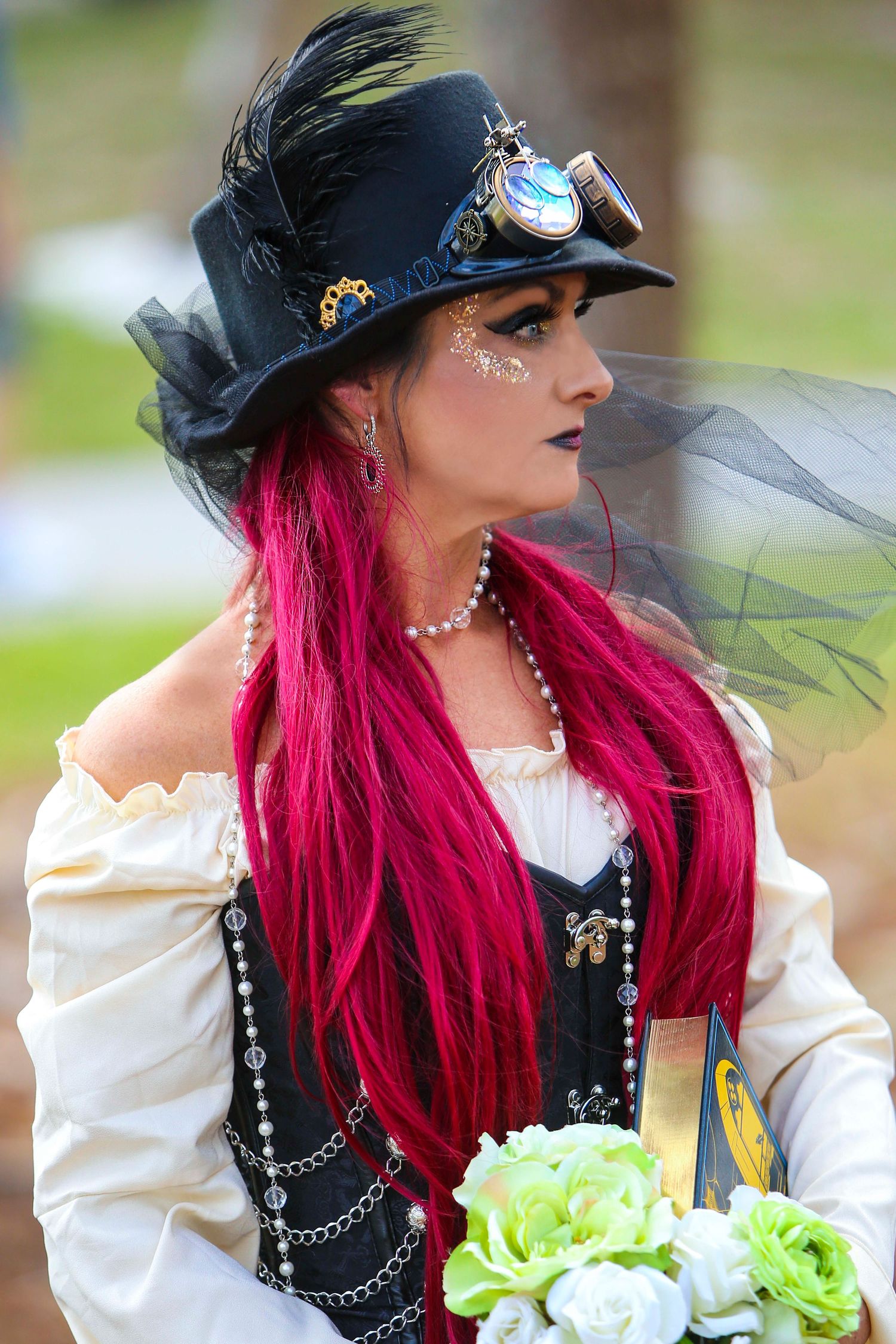 Gothic-styled person with bright red hair wearing vintage costume and pearls with floral bouquet.