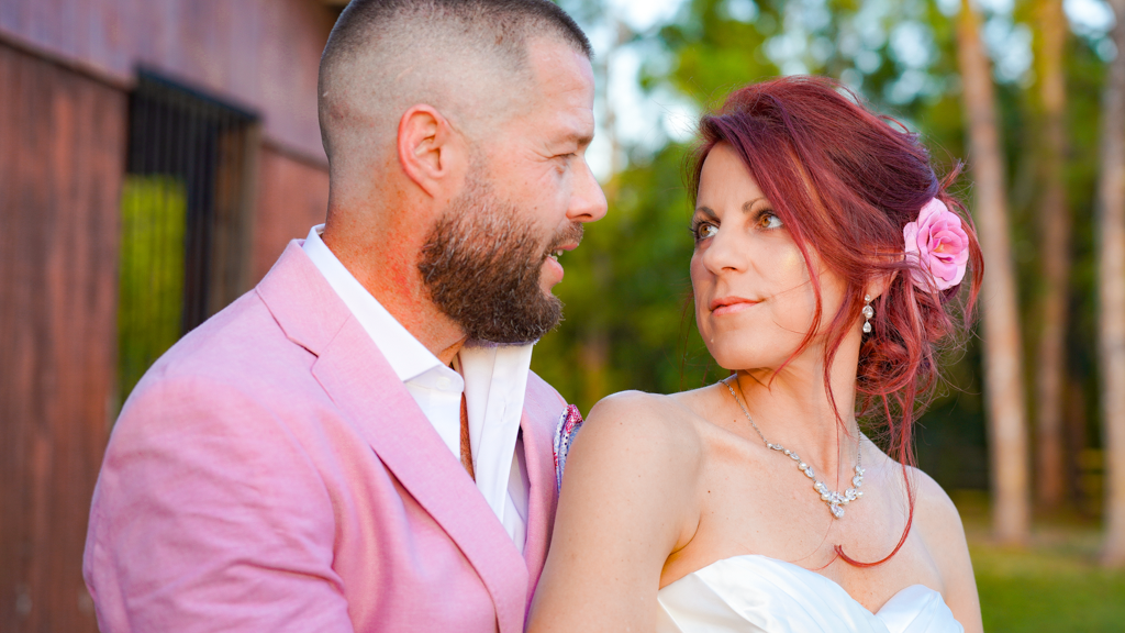 Romantic couple in pink attire sharing intimate moments in a wooded outdoor setting.