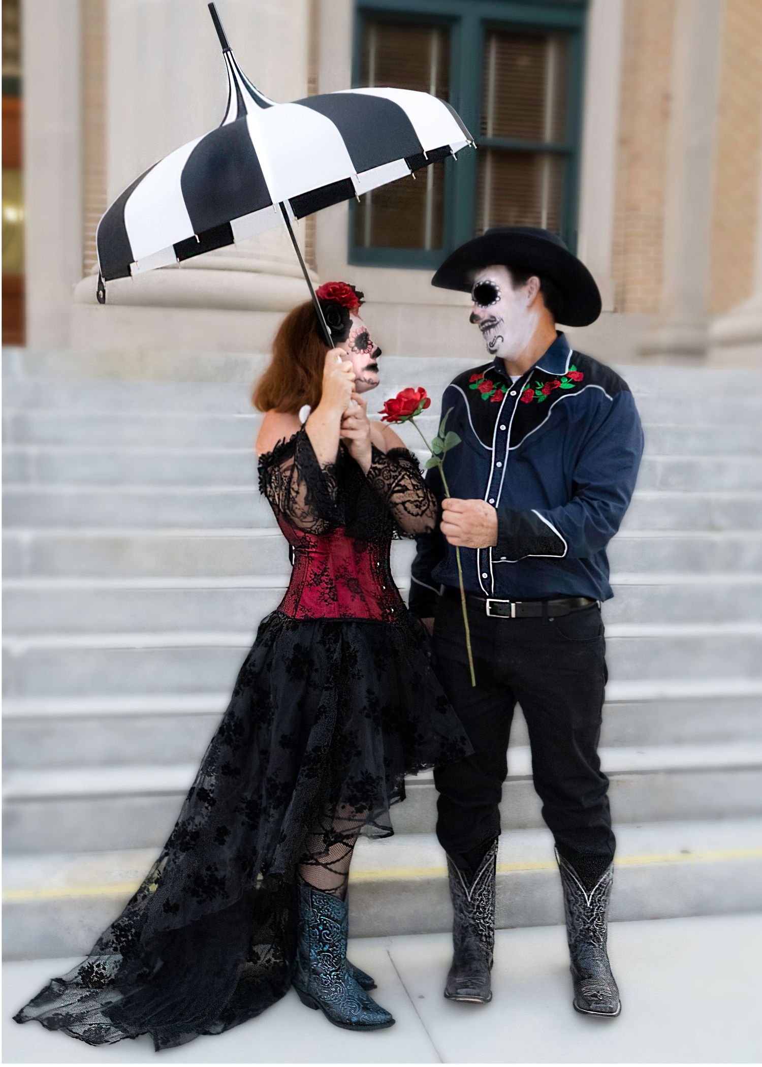 Romantic couple in vintage attire with black umbrella posing on stone steps.