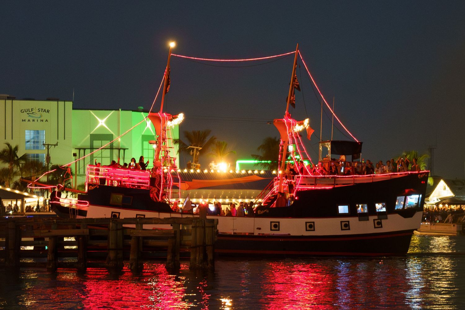 A pirate-themed boat illuminated with red lights docked at night in a harbor with reflections on the water.
