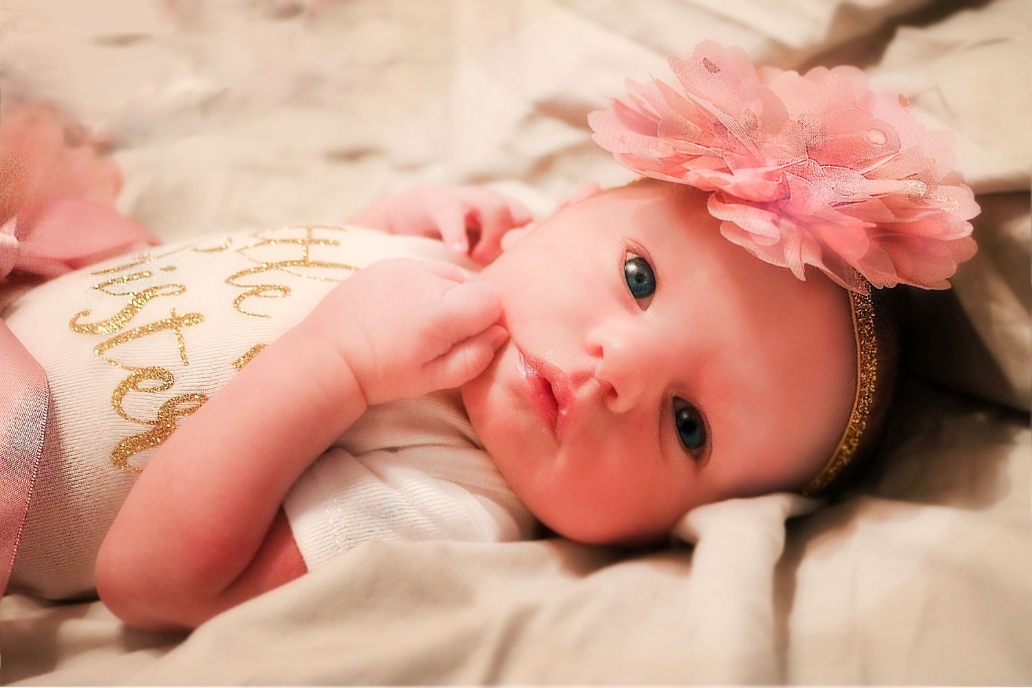 Baby wearing pink floral accessories lying on soft fabric in a series of gentle poses.