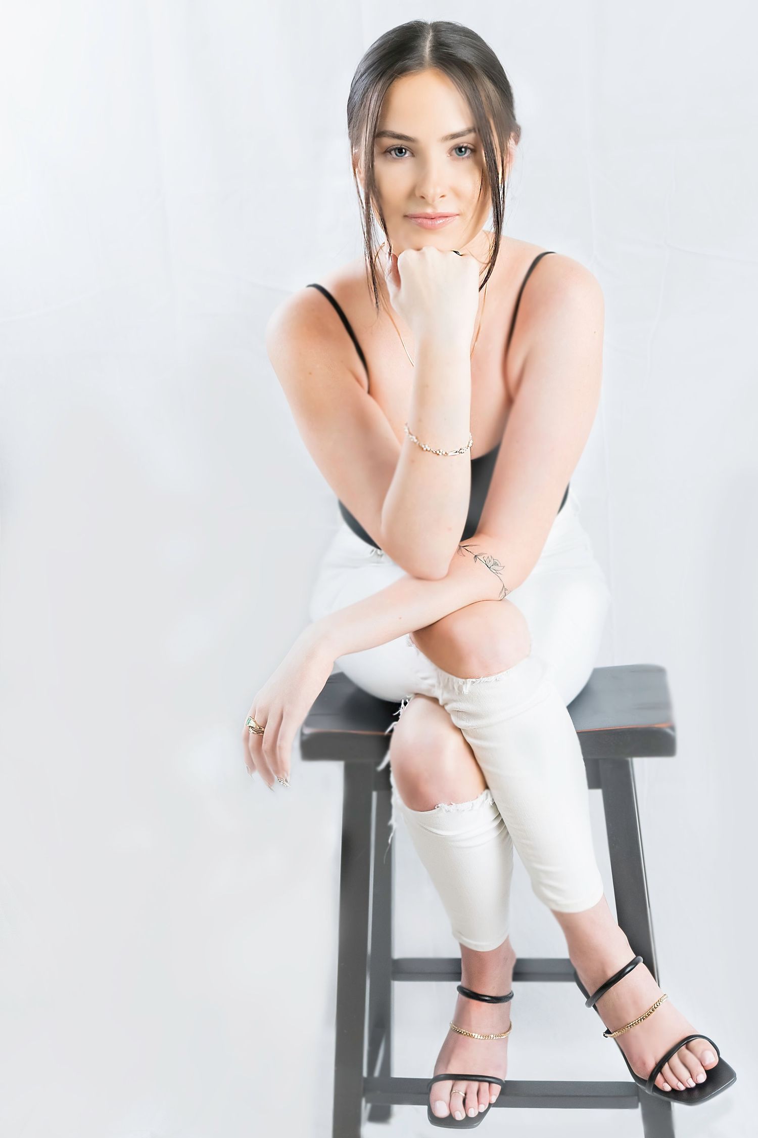 Portrait series of someone in white attire posing thoughtfully on a dark bench.