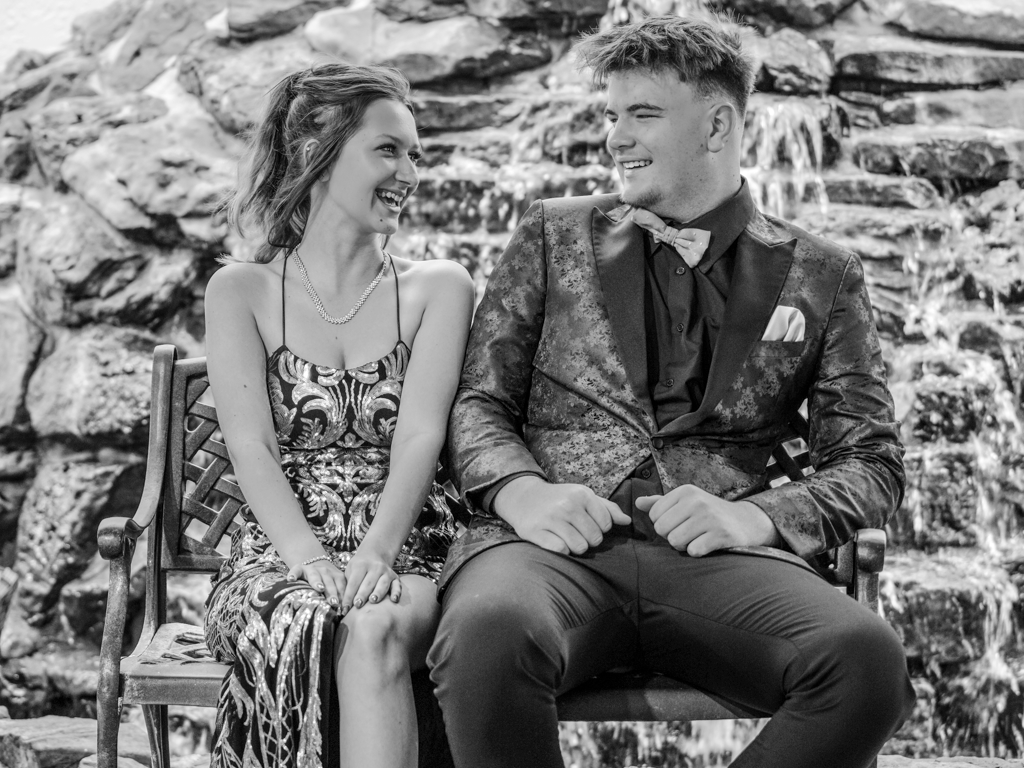 Black and white portrait of couple sitting on stone wall outdoors.