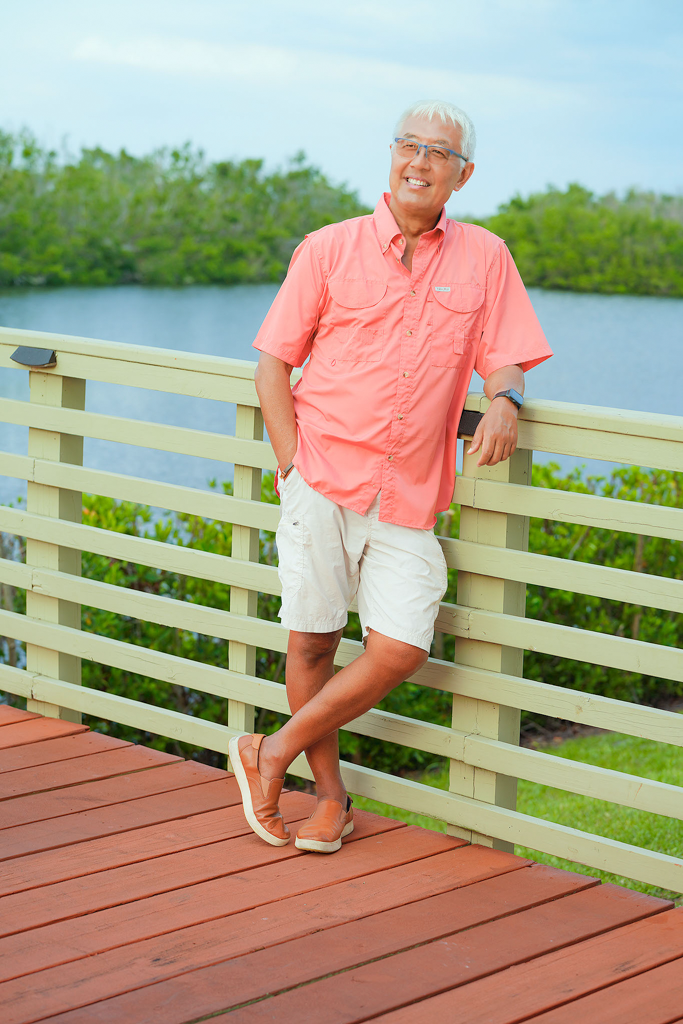 Person in coral shirt relaxing on wooden deck overlooking waterfront mangroves.