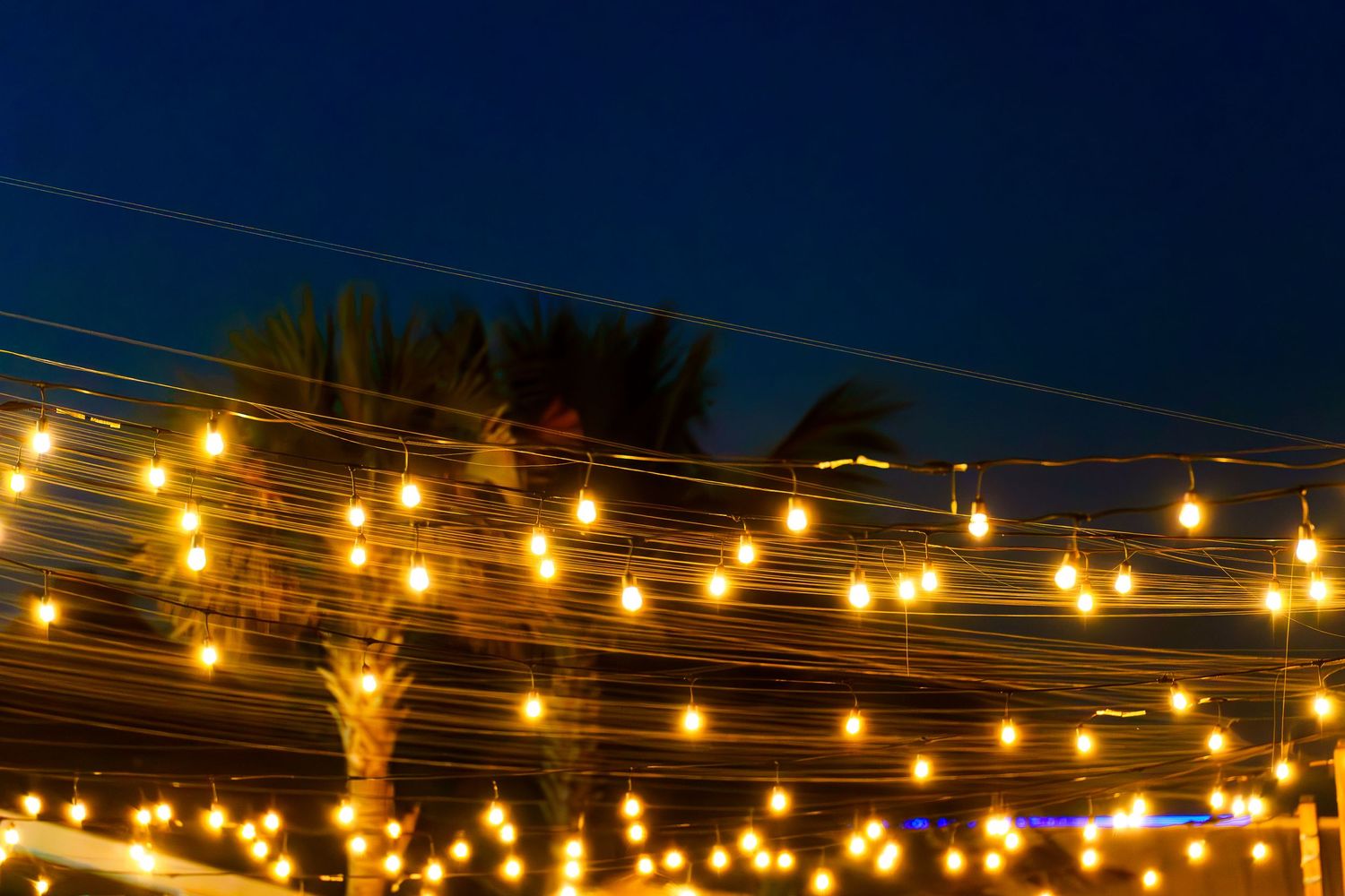 String lights illuminate a dark outdoor patio area against a twilight sky creating a warm, inviting ambiance.