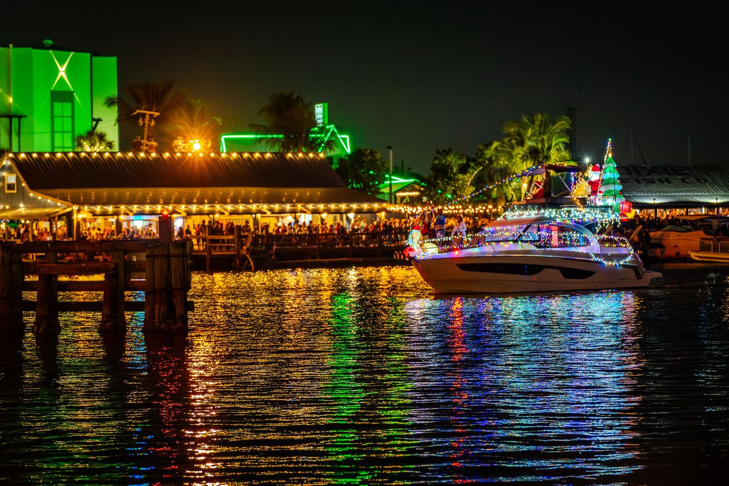 Colorful nighttime reflections of illuminated buildings and boats on dark water create a vibrant waterfront scene.