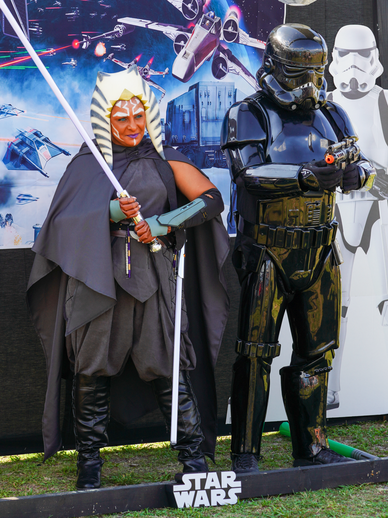 Star Wars cosplayers dressed as a Jedi and Stormtrooper pose with lightsabers against a space backdrop.