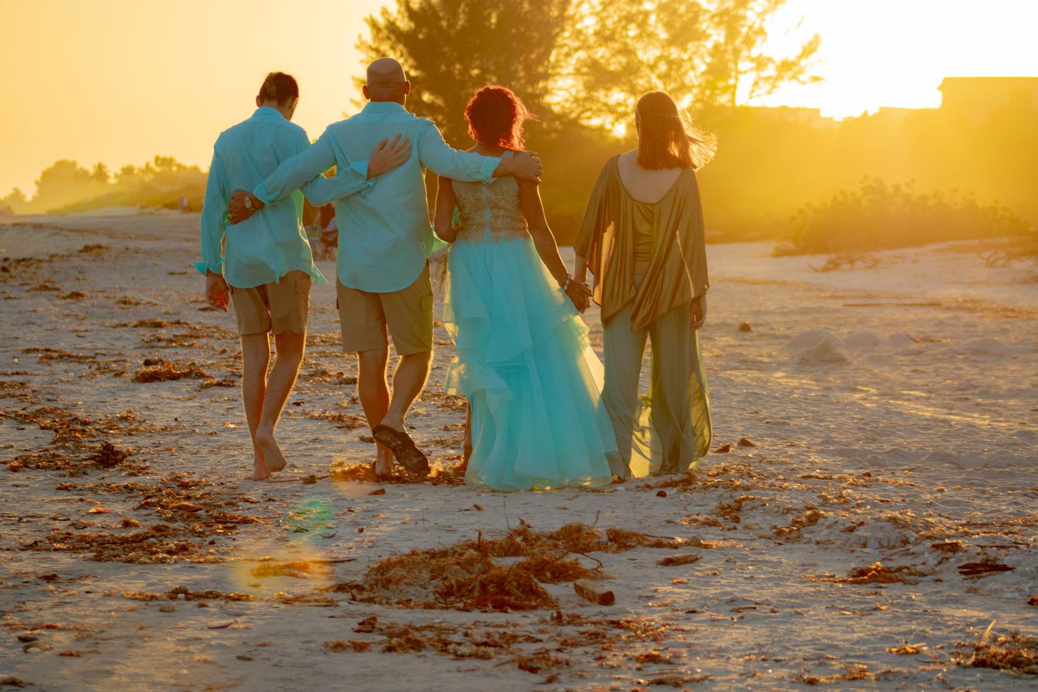 People in turquoise and mint outfits gather on a beach during golden hour.