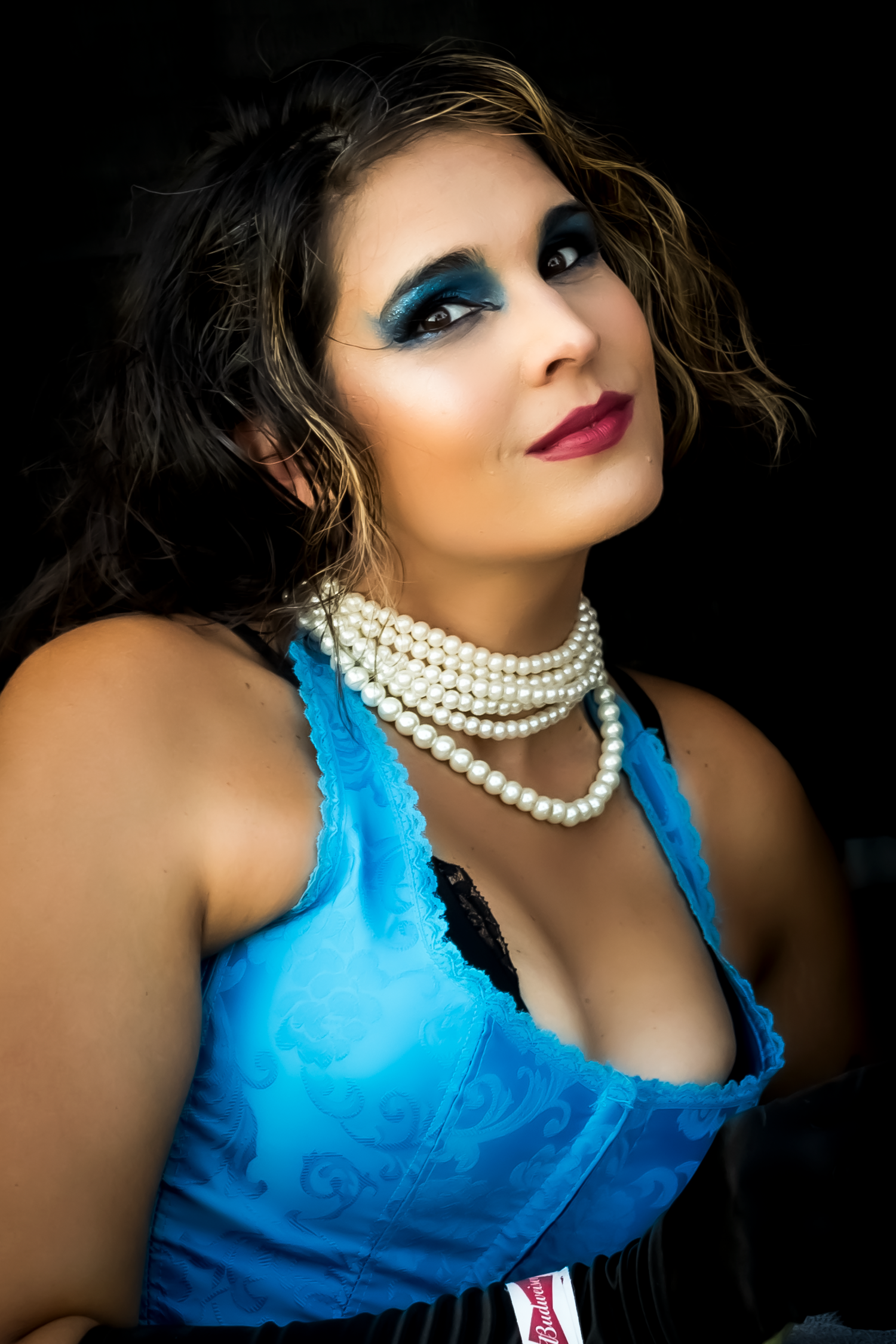 Dramatic portrait in blue satin dress with pearl necklace against black background.