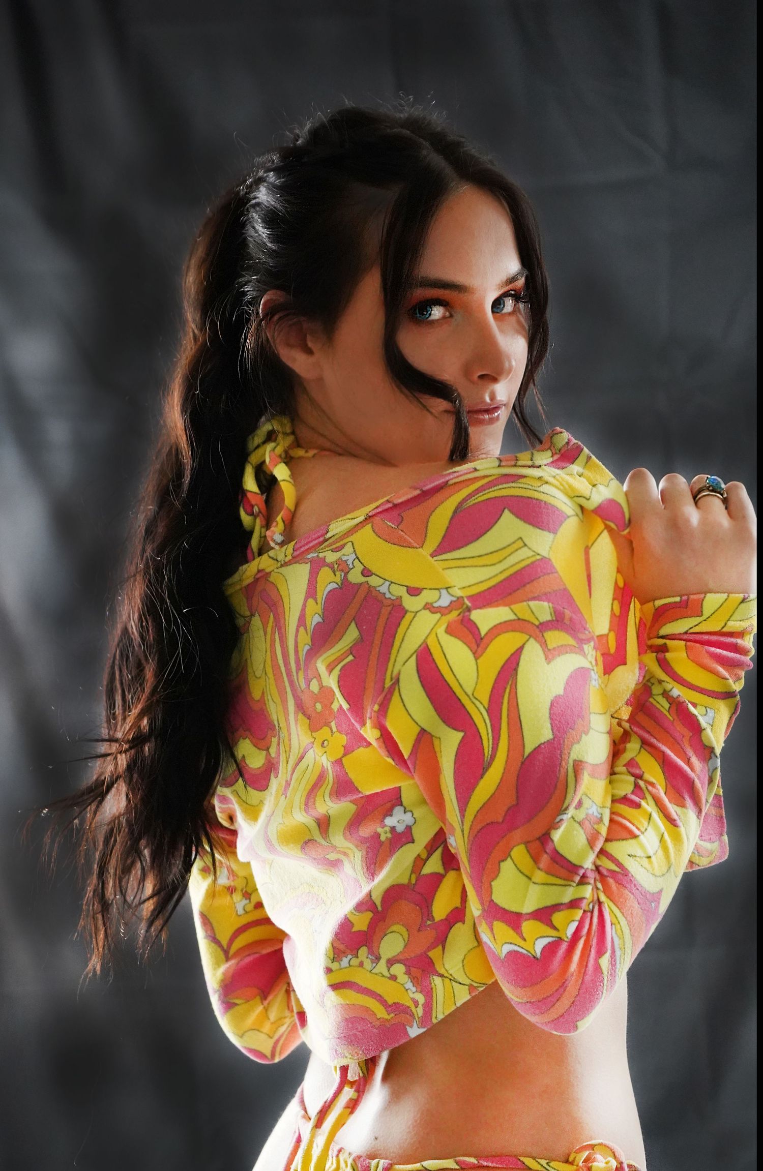 A fashion photo showing a colorful yellow and pink patterned top against a dark studio backdrop.