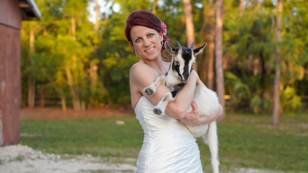 Bride in white dress posing outdoors among trees.