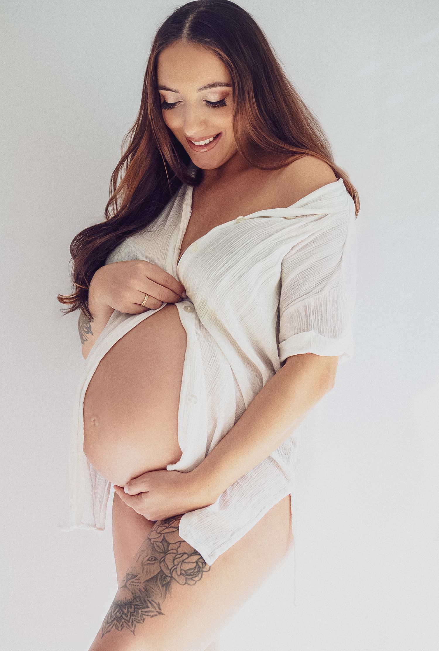 Artistic black and white maternity photo series showing a woman in a white top embracing her pregnant belly.
