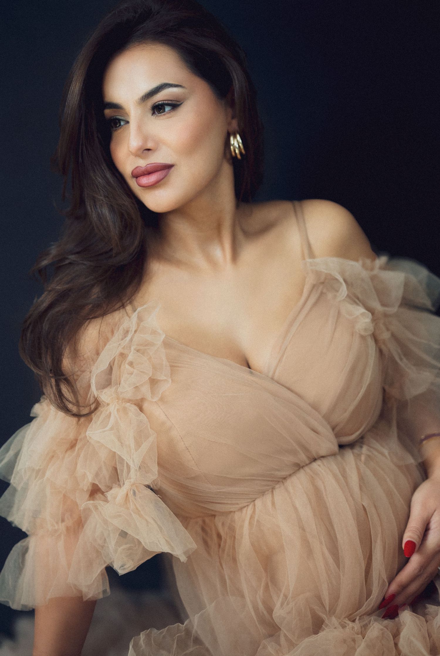 Glamorous fashion photoshoot featuring a romantic beige tulle gown against a dark background.