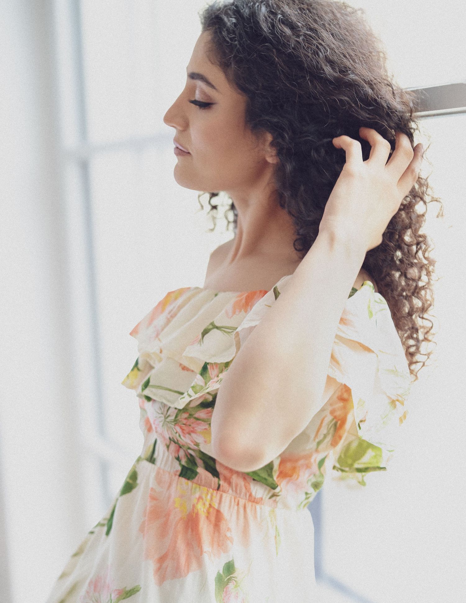 Dreamy portrait by a window featuring a floral dress and natural curls.