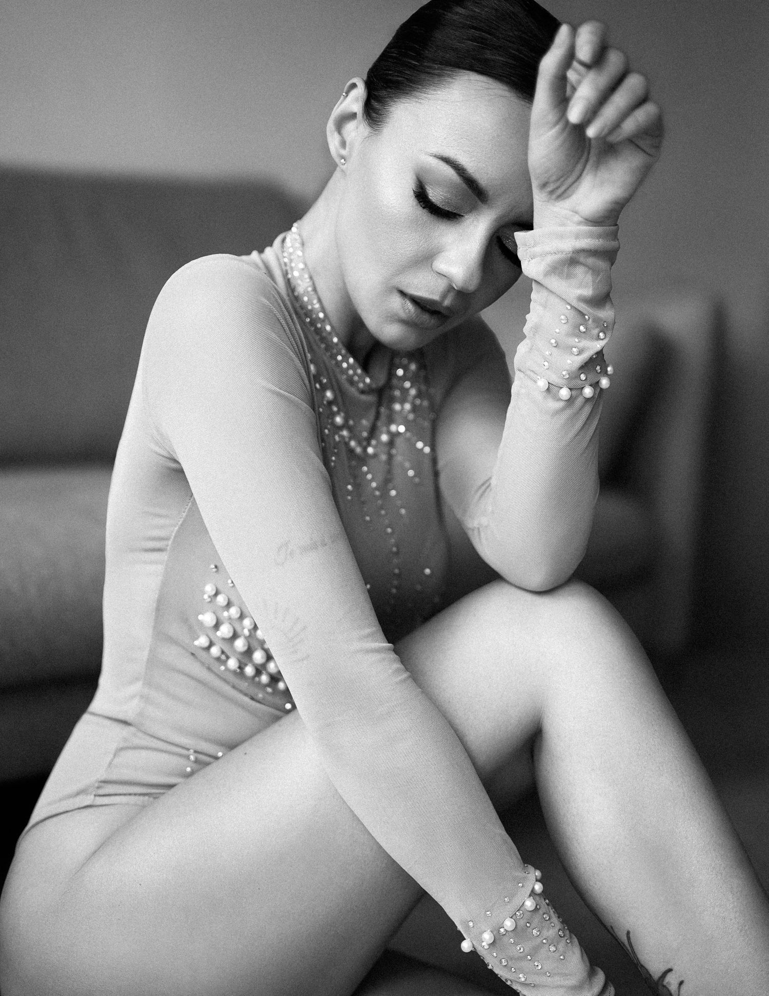 A black and white artistic portrait of a figure in an elegant rhinestone-adorned leotard in a contemplative pose.