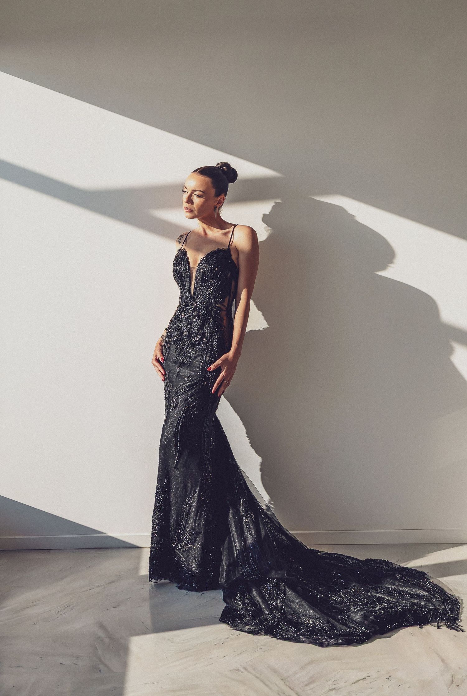 Model in stunning black sequin mermaid gown with train, posing in sunlit minimalist room.