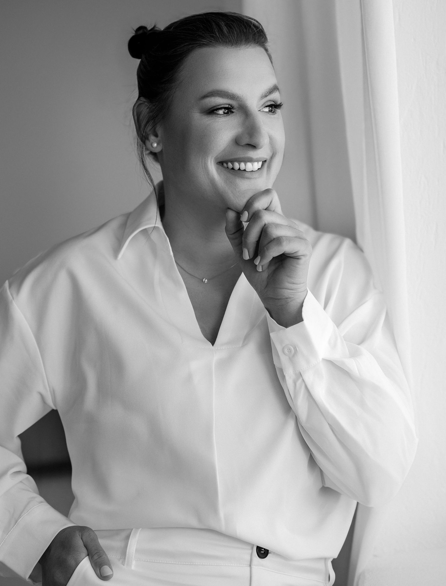 Smiling woman in white button-up shirt poses confidently in black and white portrait photo.