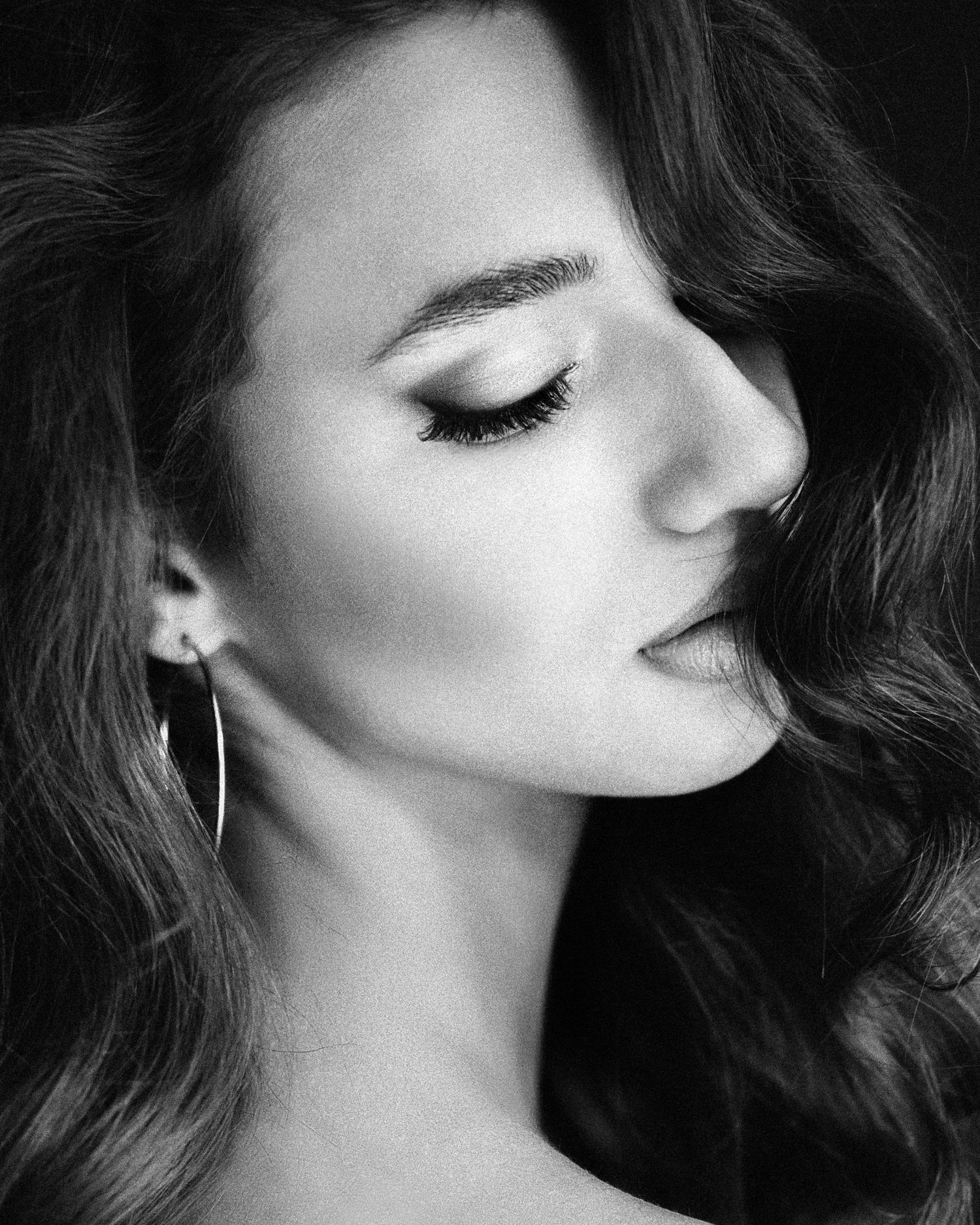 Black and white profile portrait of a young woman with wavy hair wearing hoop earrings, eyes closed.