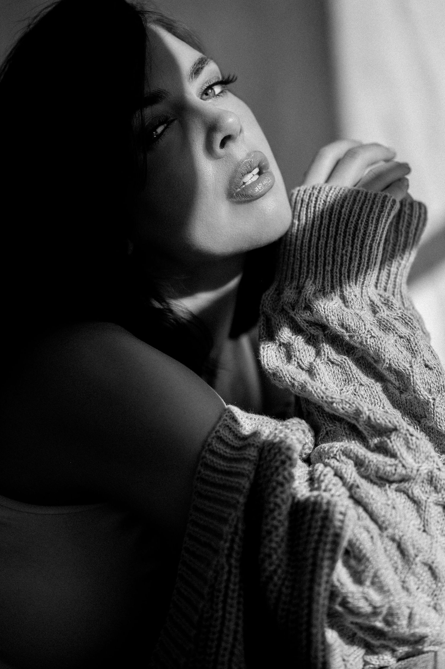 Dramatic black and white portrait showing contemplative expression in cozy knit sweater with moody lighting.