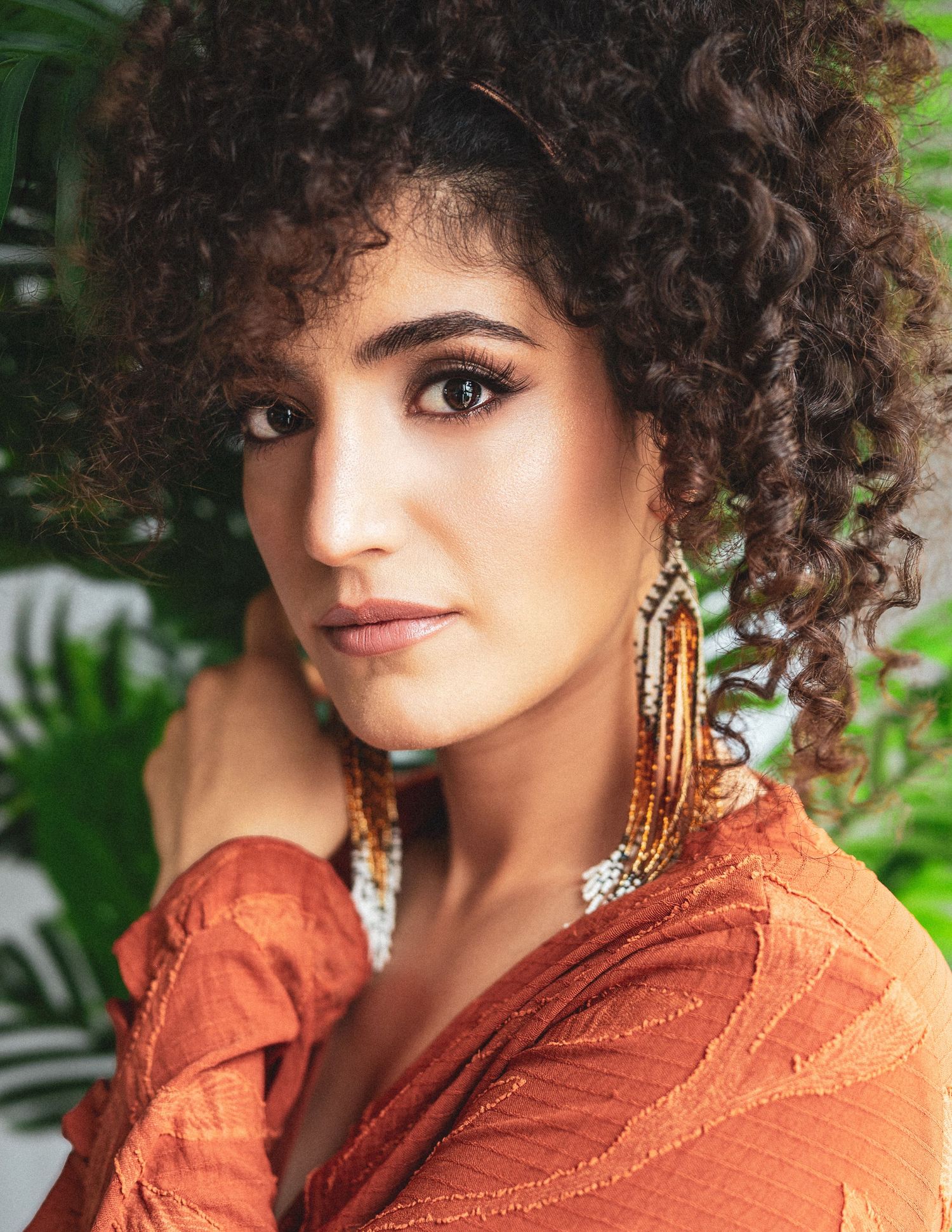 Fashion portrait of someone with natural curly hair wearing a rust-colored top and statement earrings.