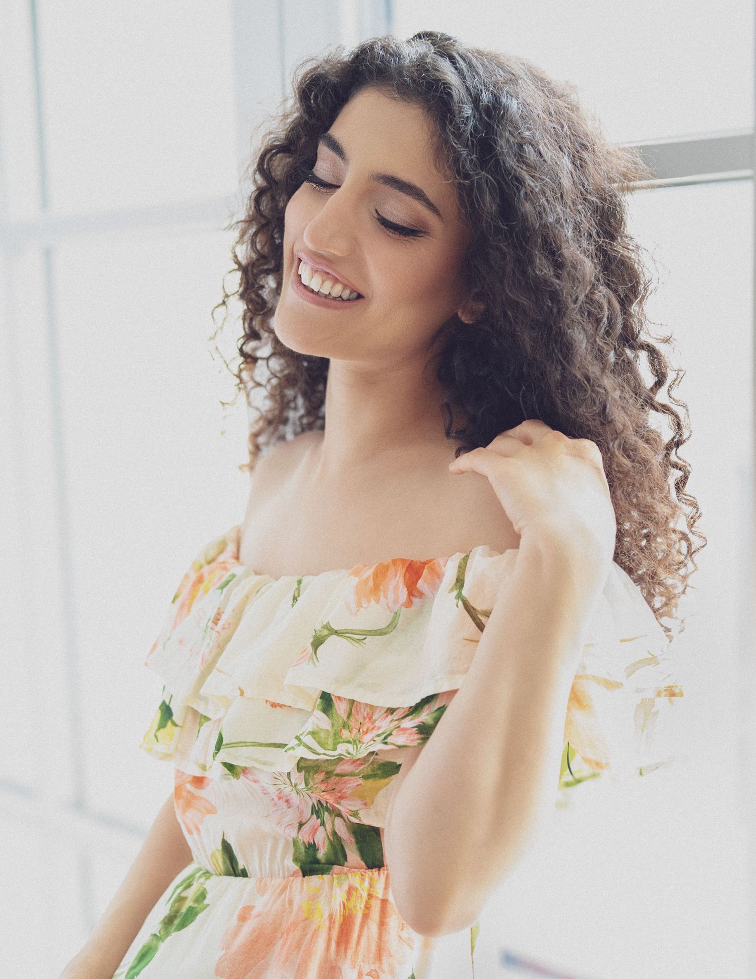 Portrait in a bright room showing someone in a floral dress with curly hair.