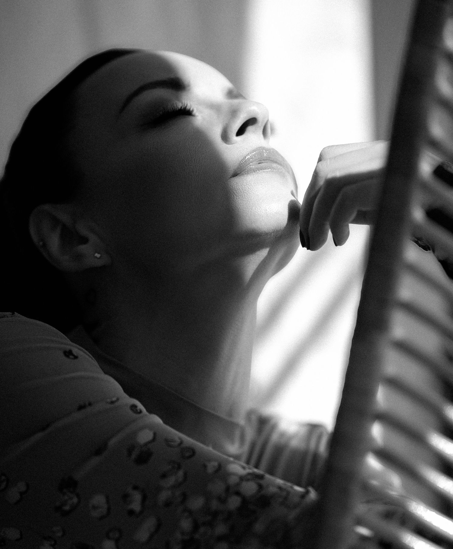Black and white portrait of a woman resting her chin on her hand, gazing upward in soft dramatic lighting.