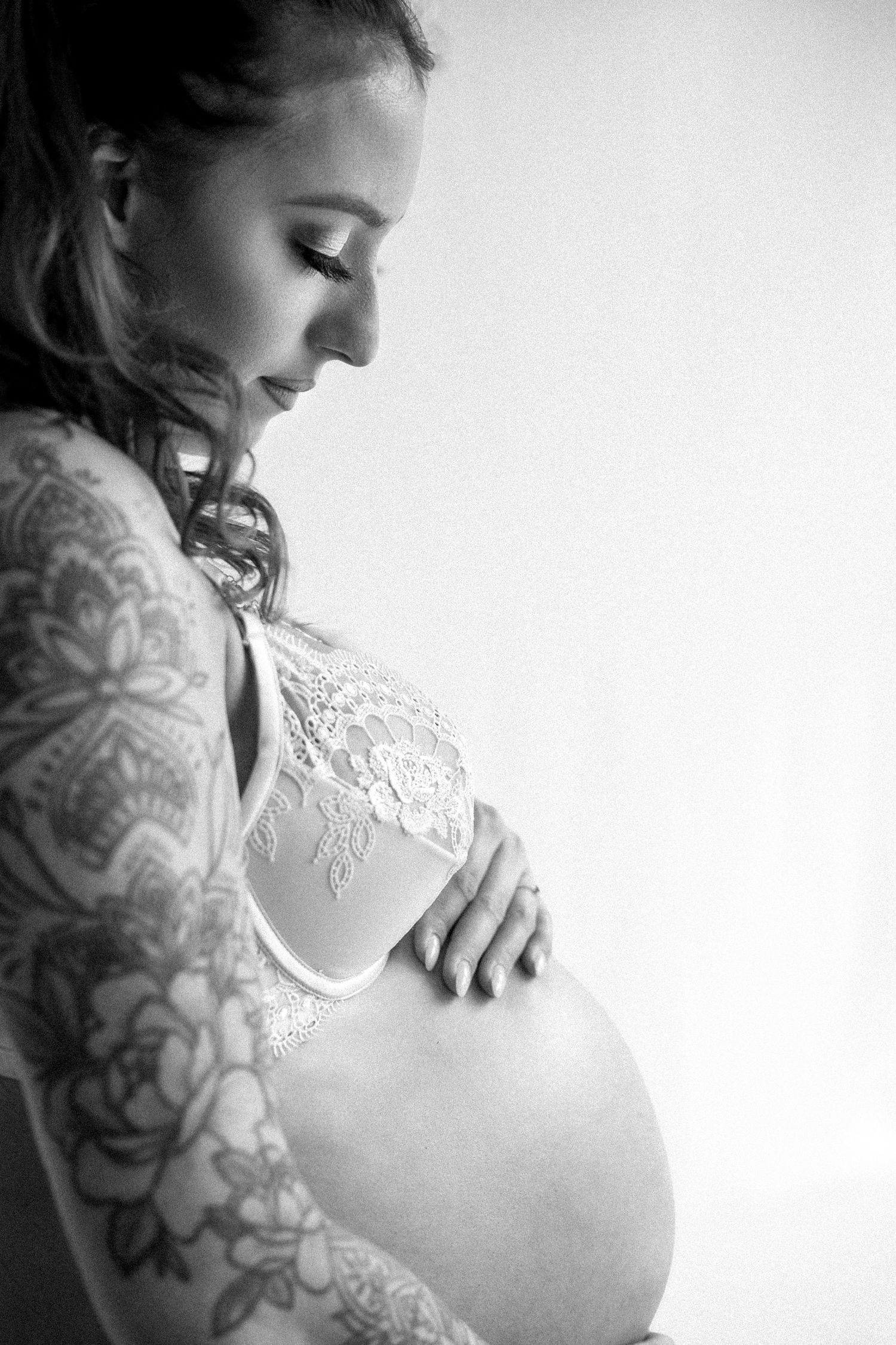 Black and white maternity photos showing a pregnant belly with delicate lace details and tattoos.