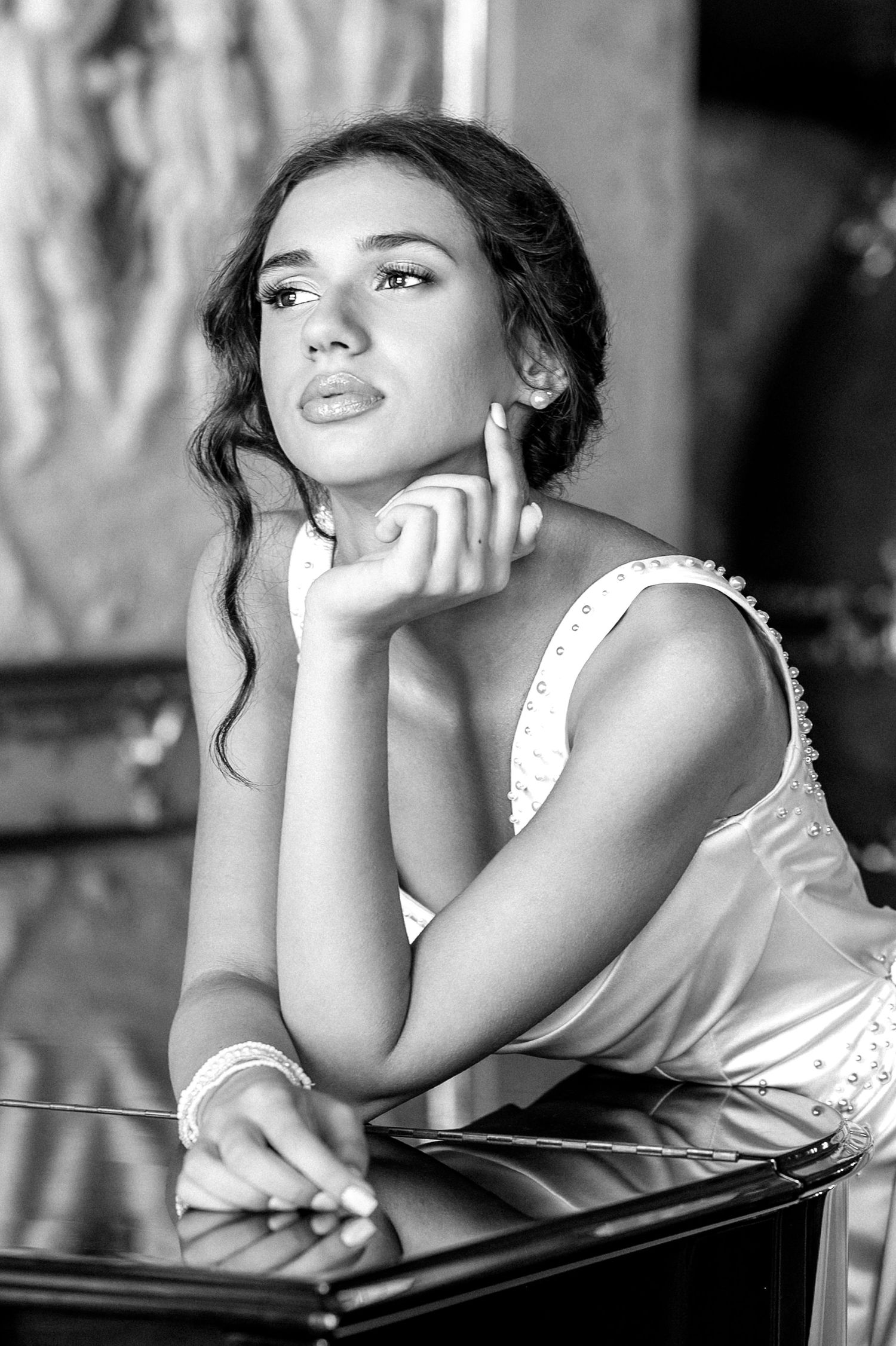 Black and white portrait of a young woman in a white dress, resting her chin on her hand with a contemplative expression.